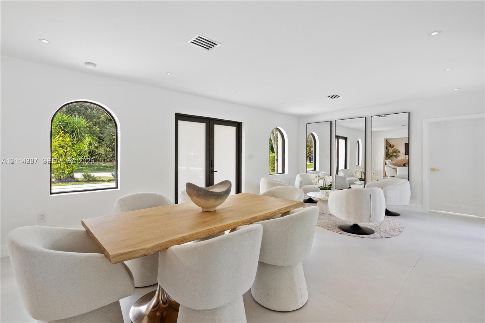 Light-filled room featuring large-format tile flooring, recessed lighting, arched window frames, and glass-paneled double doors with dark framing