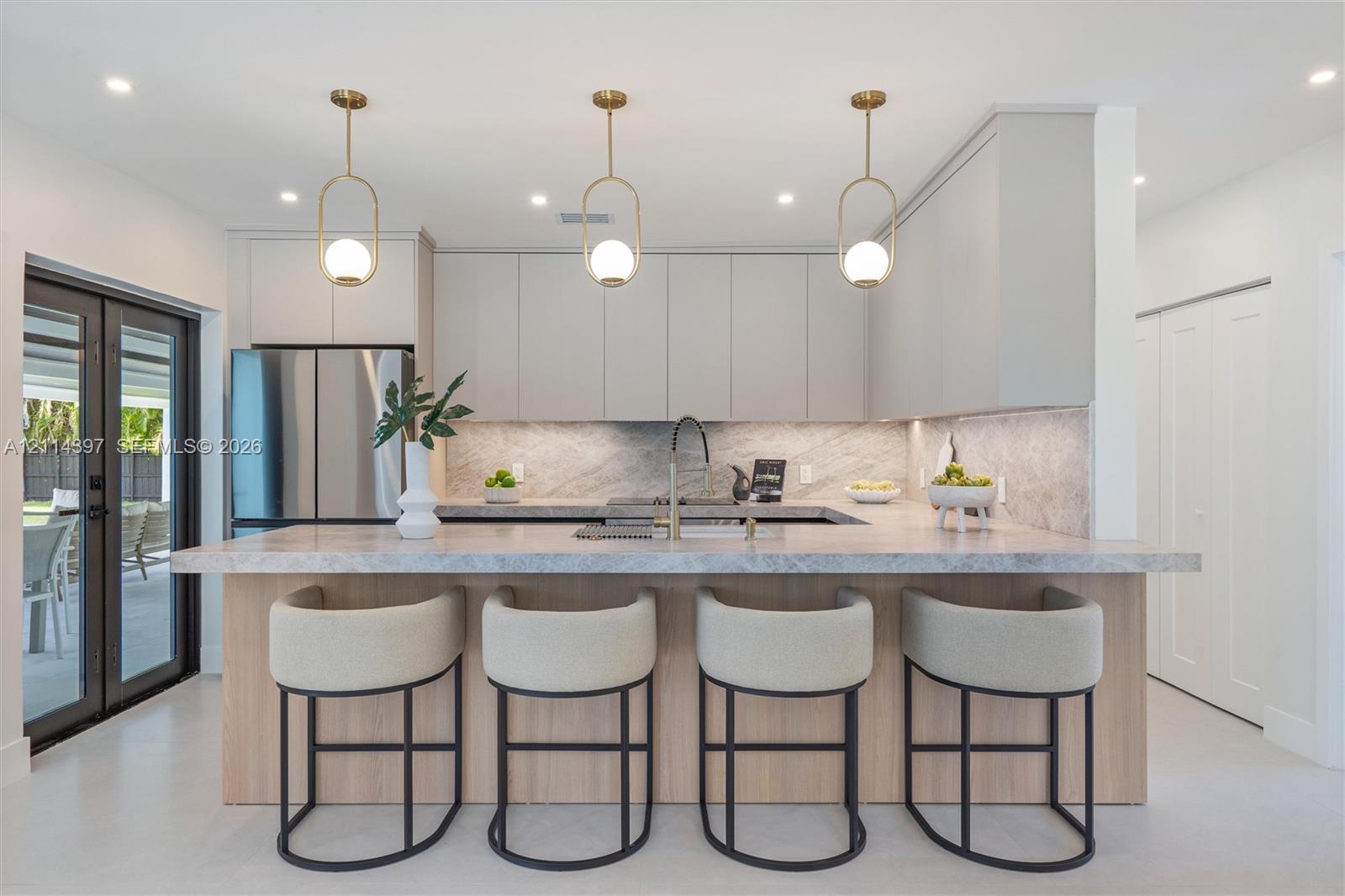 Kitchen featuring flat-panel cabinetry, a stone-surfaced kitchen island, three pendant light fixtures, stainless steel refrigerator, and a gooseneck faucet