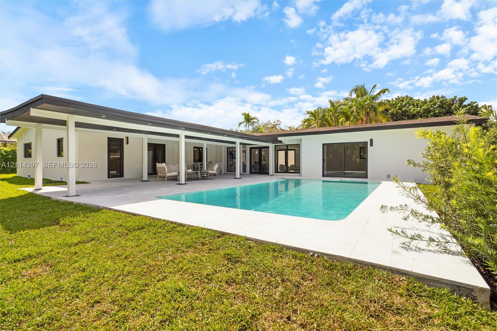 Exterior featuring a spacious covered patio, a rectangular in-ground swimming pool, light-toned stone pool decking, and white stucco siding
