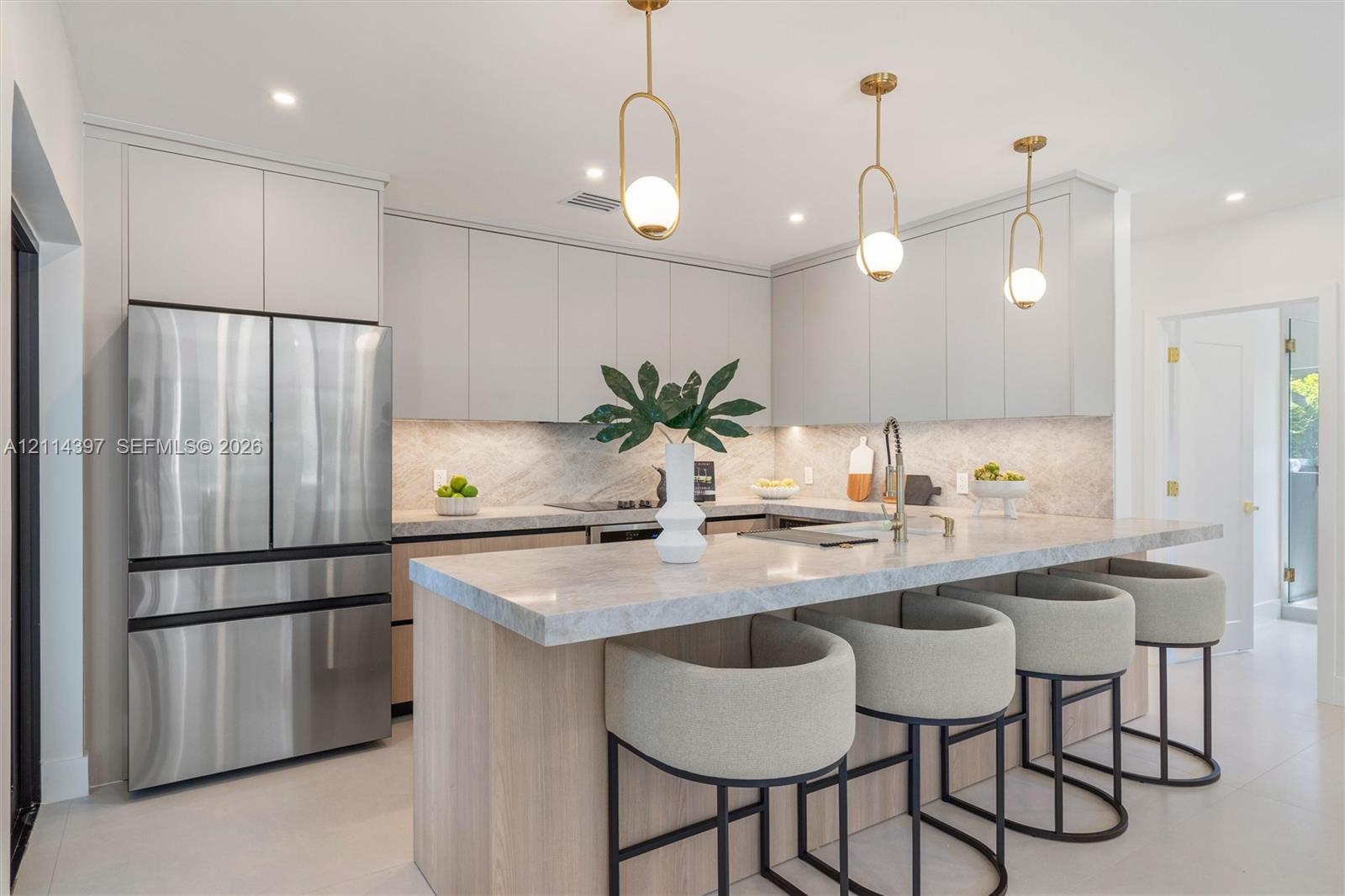 Kitchen featuring light wood-finish cabinetry, stone countertops and backsplash, stainless steel refrigerator, and three brass-finish pendant lights