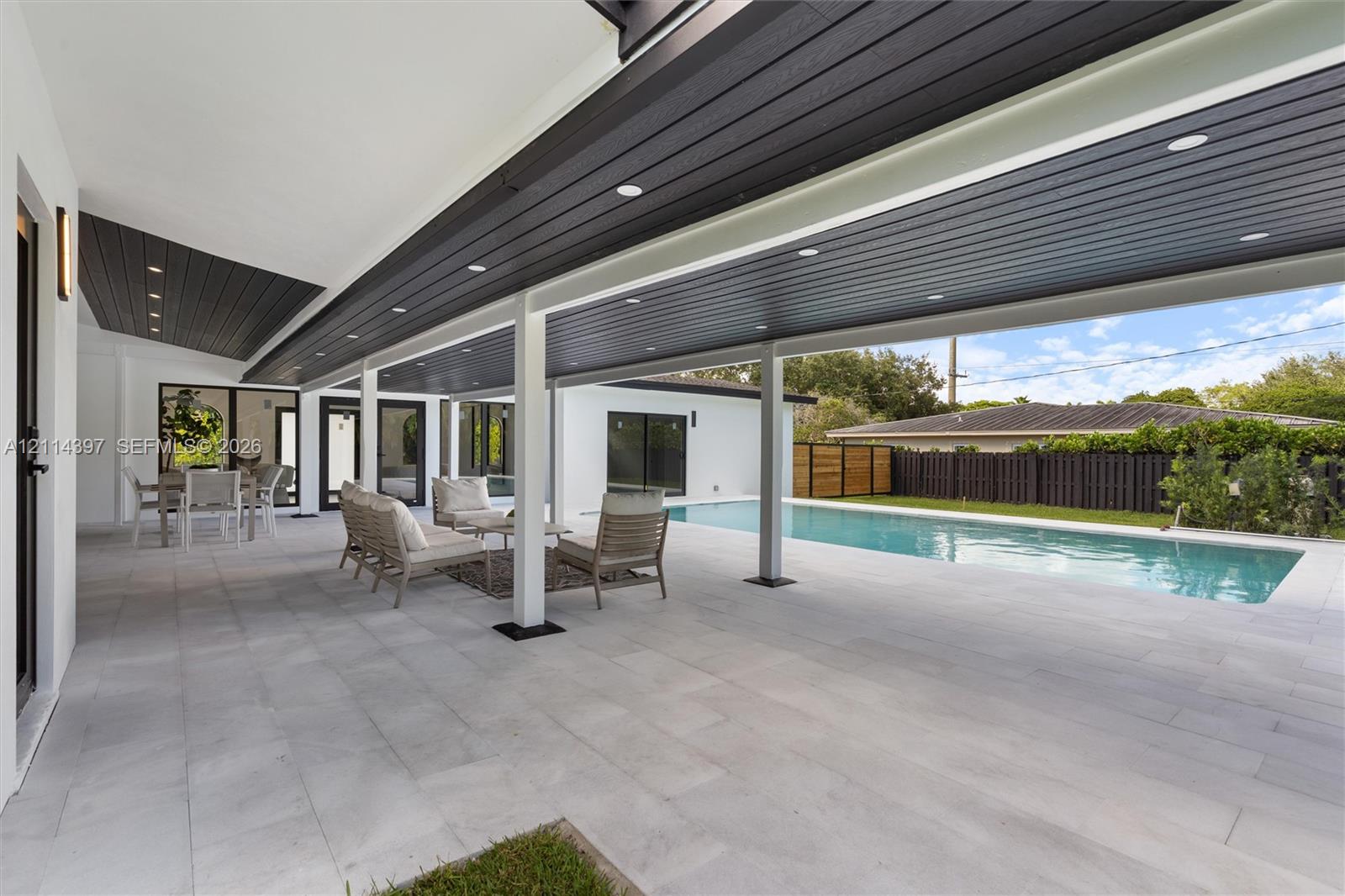 Covered outdoor patio featuring large-format tile flooring, recessed ceiling lighting, and a wood-finish ceiling, overlooking a rectangular swimming pool with integrated hardscaping