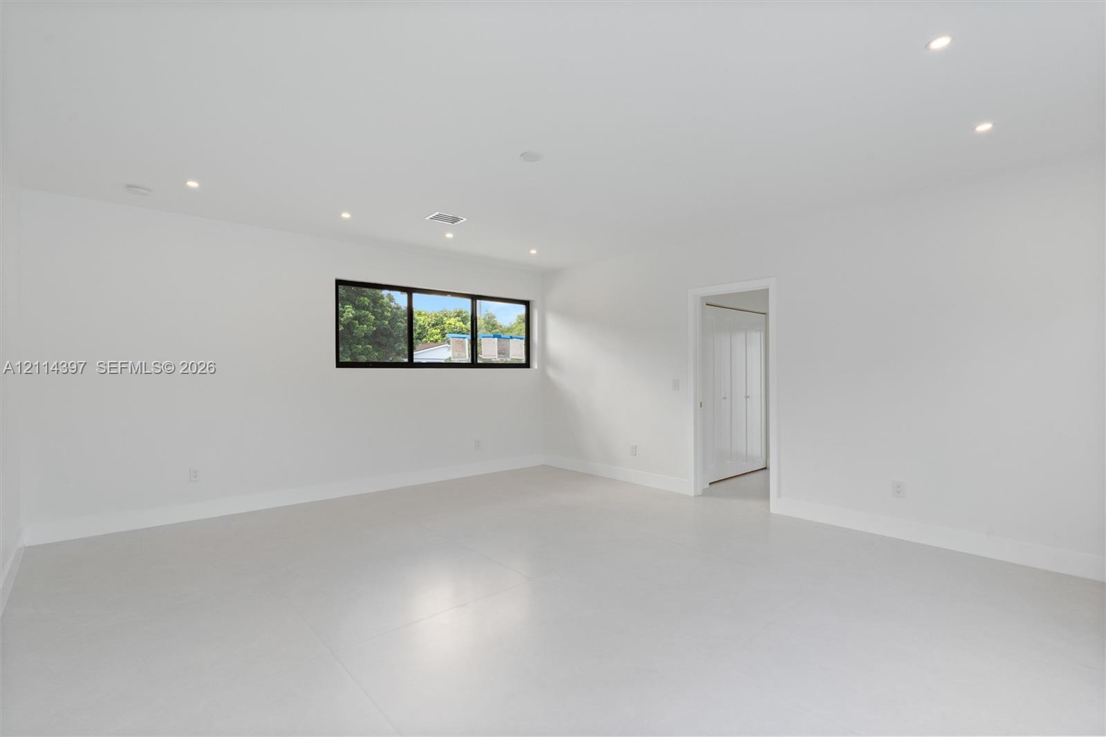 Minimalist room featuring neutral large-format tile flooring, recessed ceiling lighting, and a horizontal window with a dark frame