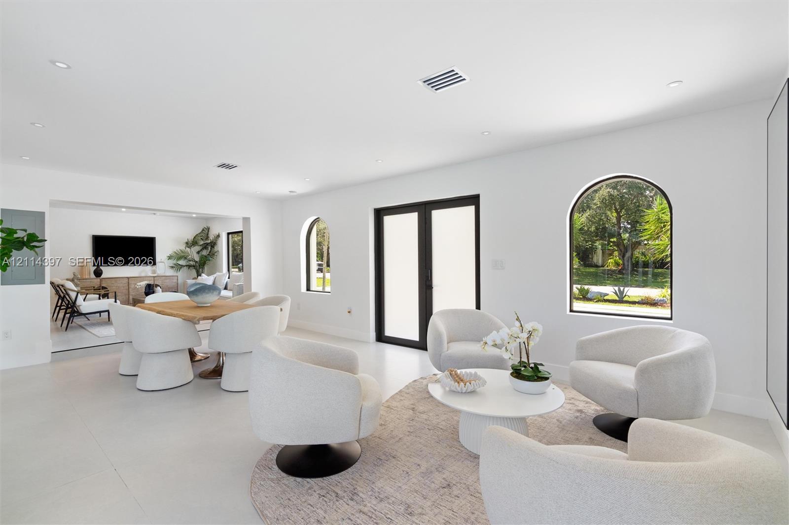 Open-concept interior featuring light-toned flooring, recessed lighting, arched window detailing, and glass-paned double doors with dark frames