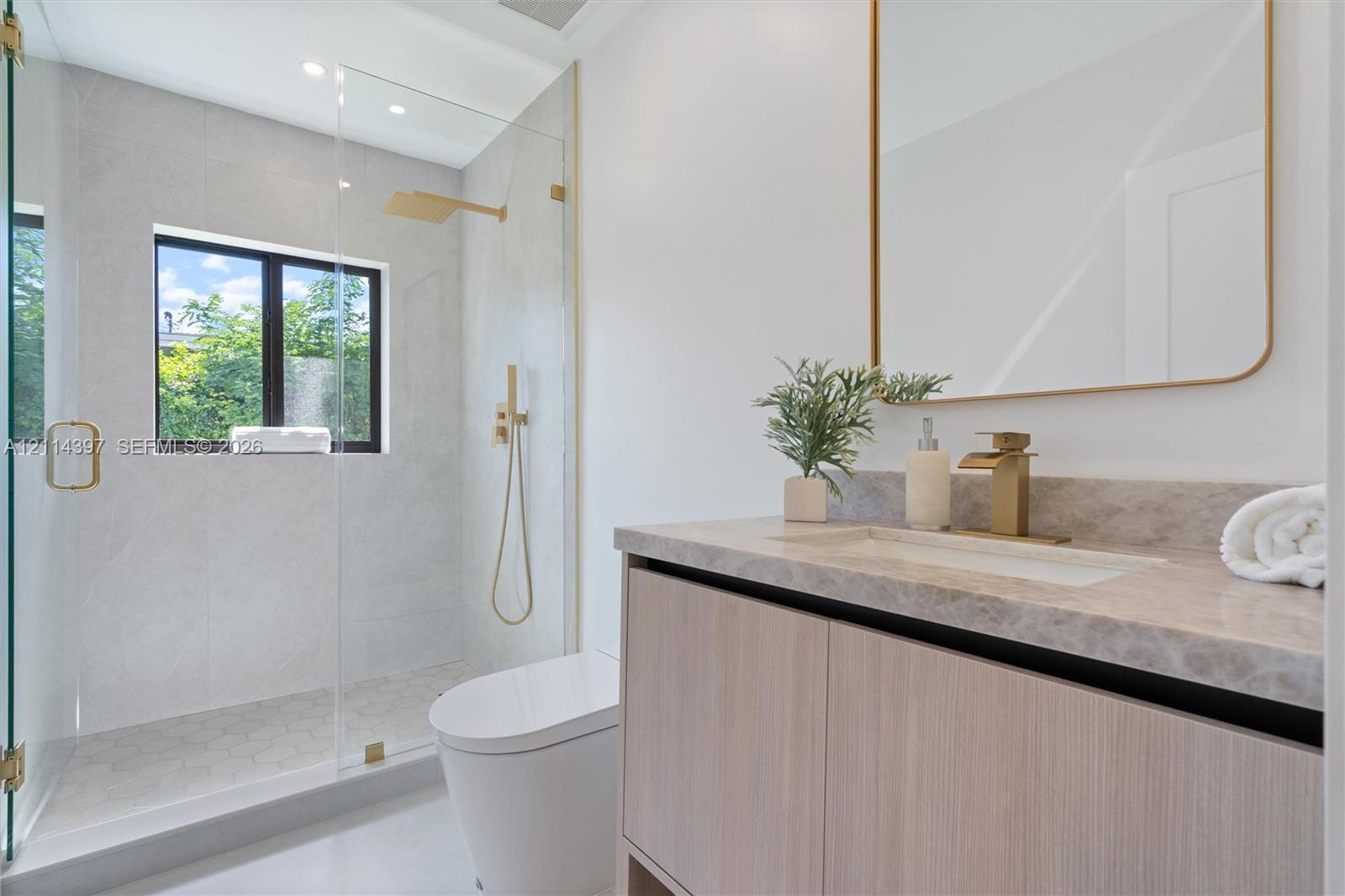 Modern vanity with stone-finish countertop, undermount sink, brass-tone hardware, wall-mounted mirror, and glass-enclosed walk-in shower with rainfall showerhead