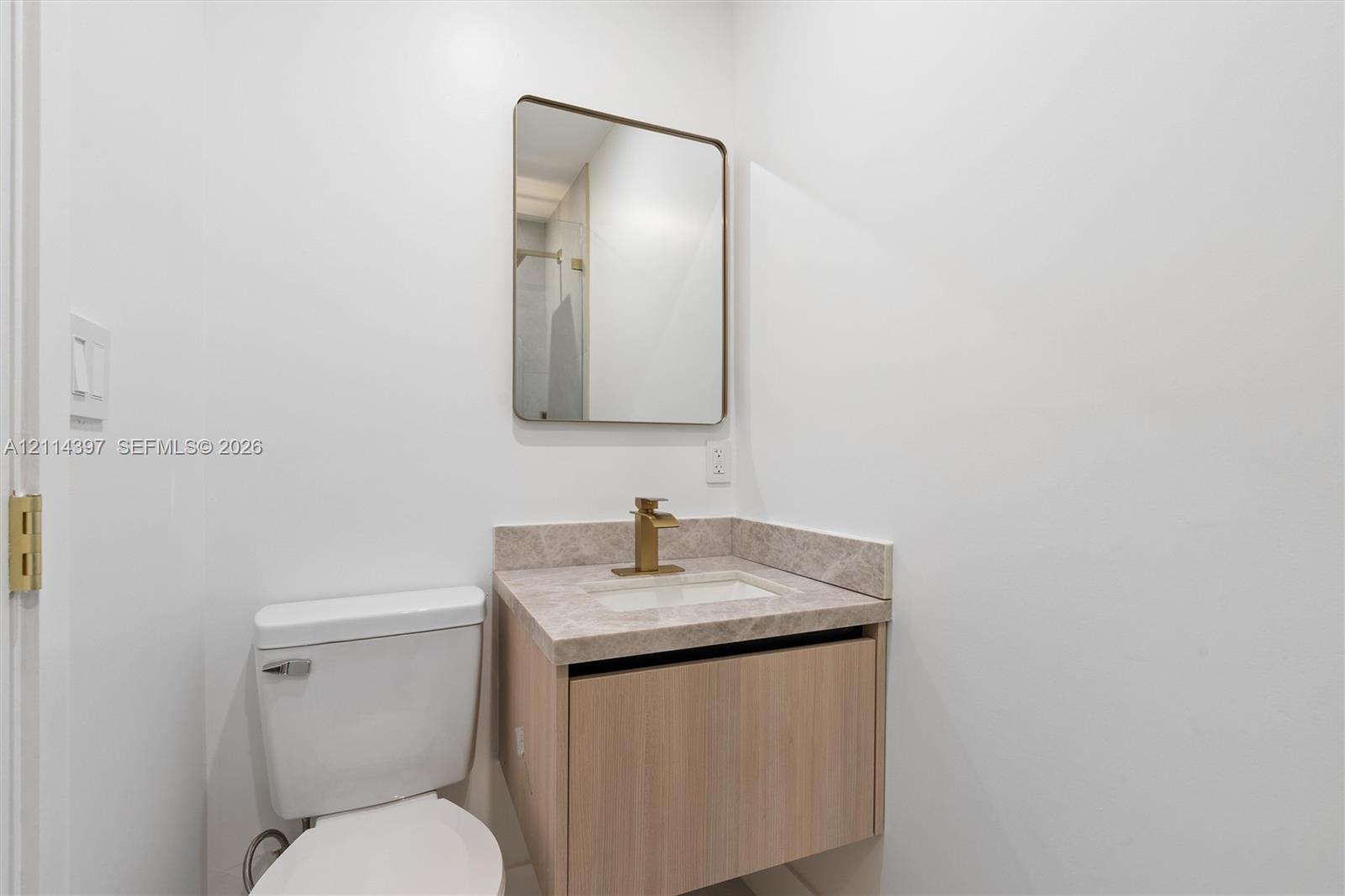 Floating vanity with a stone-finish countertop, undermount rectangular sink, brass-finish faucet, and rectangular wall-mounted mirror
