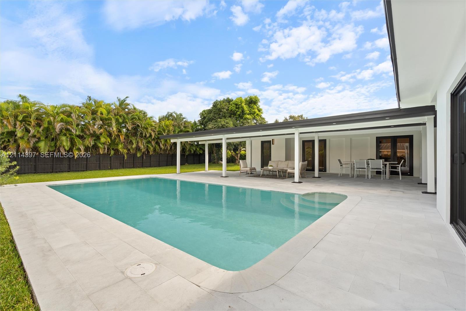 Rectangular swimming pool featuring integrated steps, expansive stone-paver decking, and a covered lanai with recessed lighting