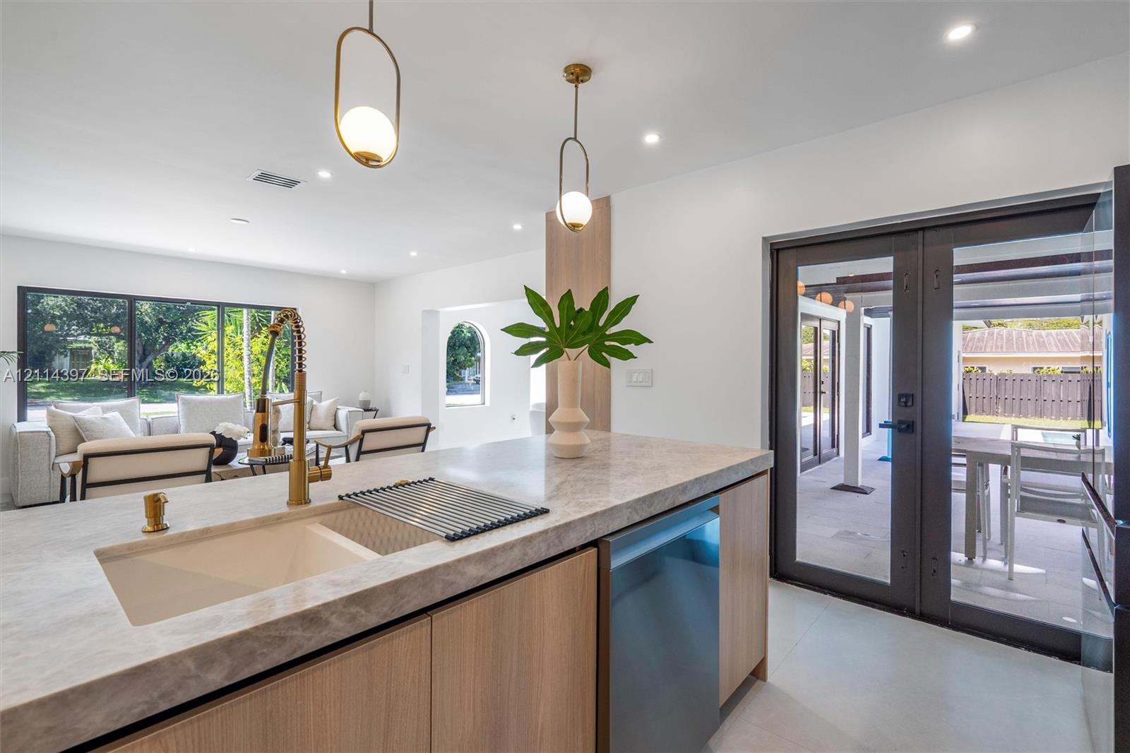 Kitchen island featuring stone-finish countertops, wood-finish cabinetry, an undermount sink with a brass-finish faucet, and modern pendant lighting