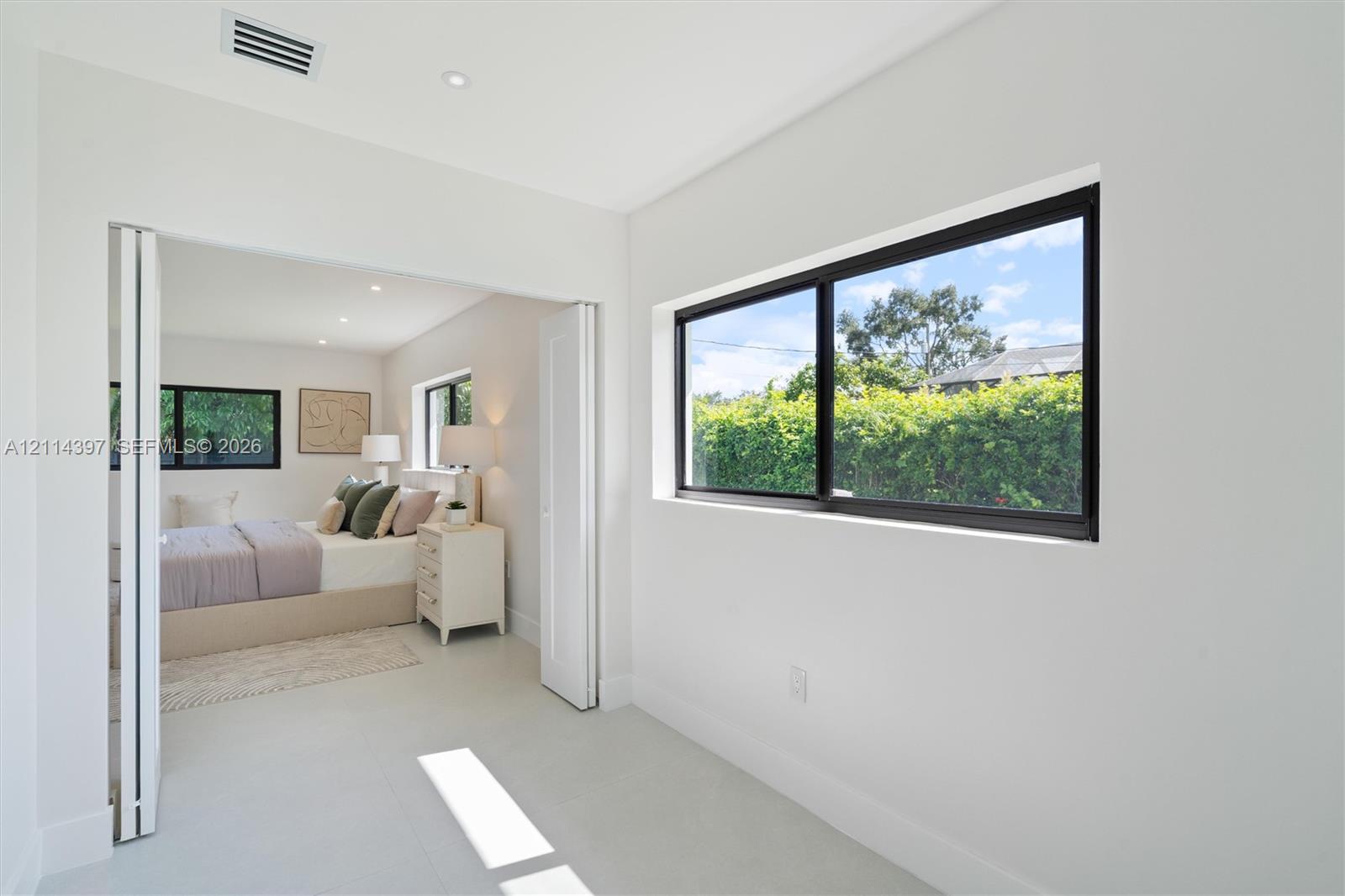 Interior space featuring light-toned flooring, neutral wall finishes, black-framed horizontal windows, and white bifold doors