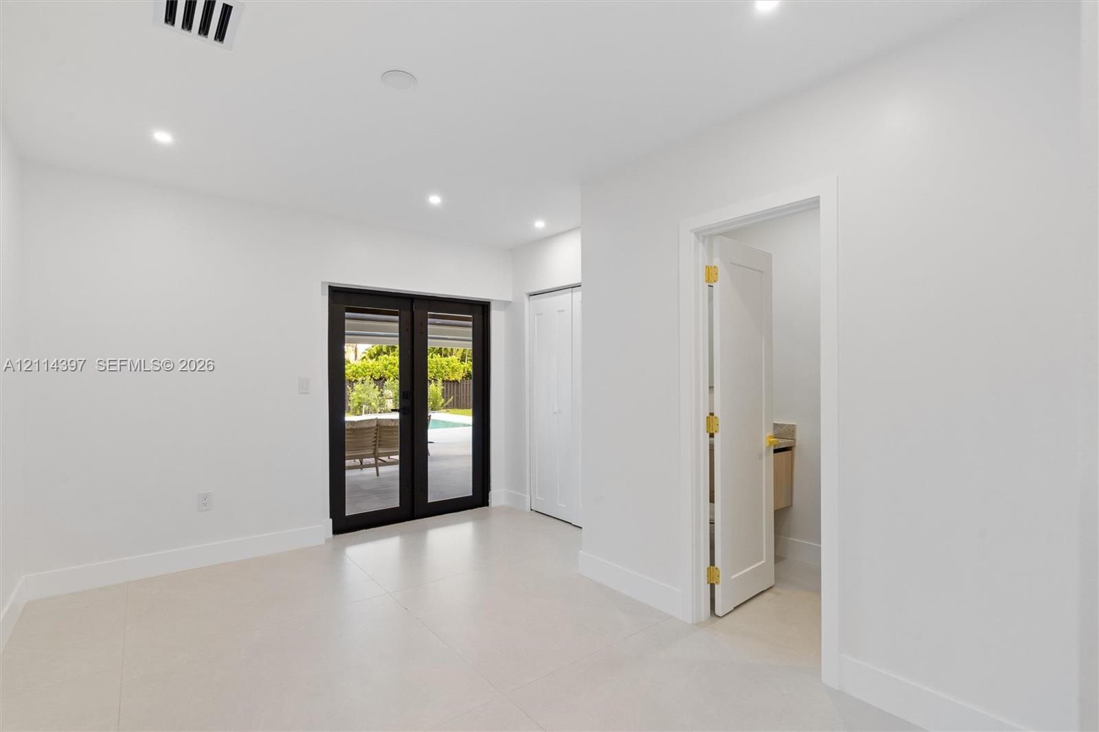 Interior space featuring light-toned tile flooring, recessed ceiling lighting, a closet with double-panel doors, and black-framed French doors