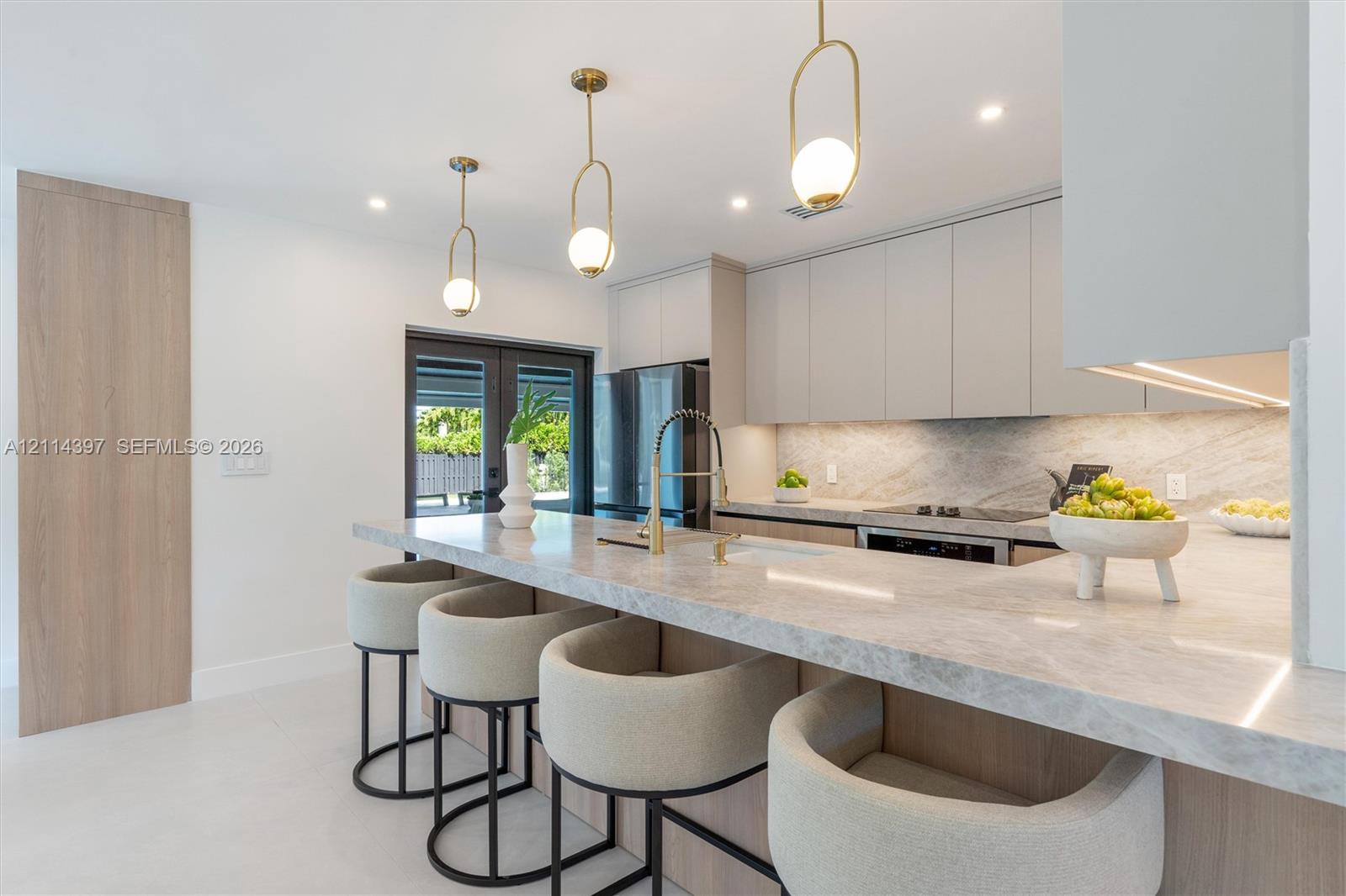 Kitchen featuring a waterfall-edge stone countertop, custom flat-panel cabinetry, gold-finish pendant lighting, and an integrated appliance package