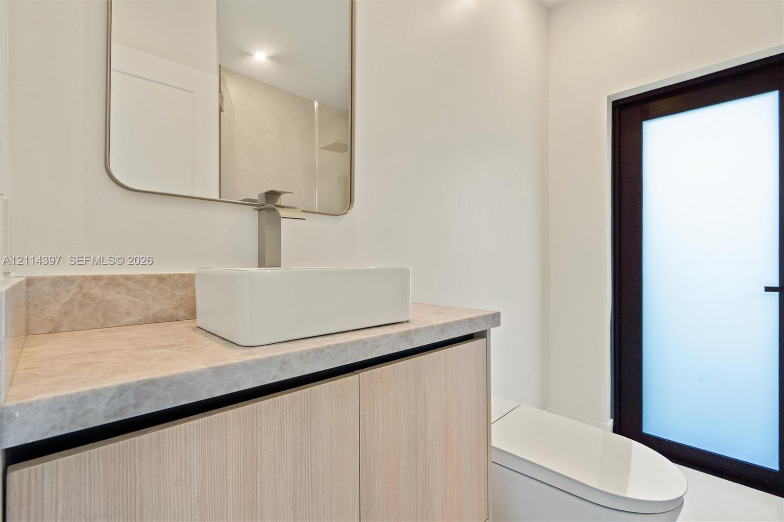 Wood-finish floating vanity with a stone countertop, rectangular vessel sink, polished metal faucet, and wall-mounted mirror