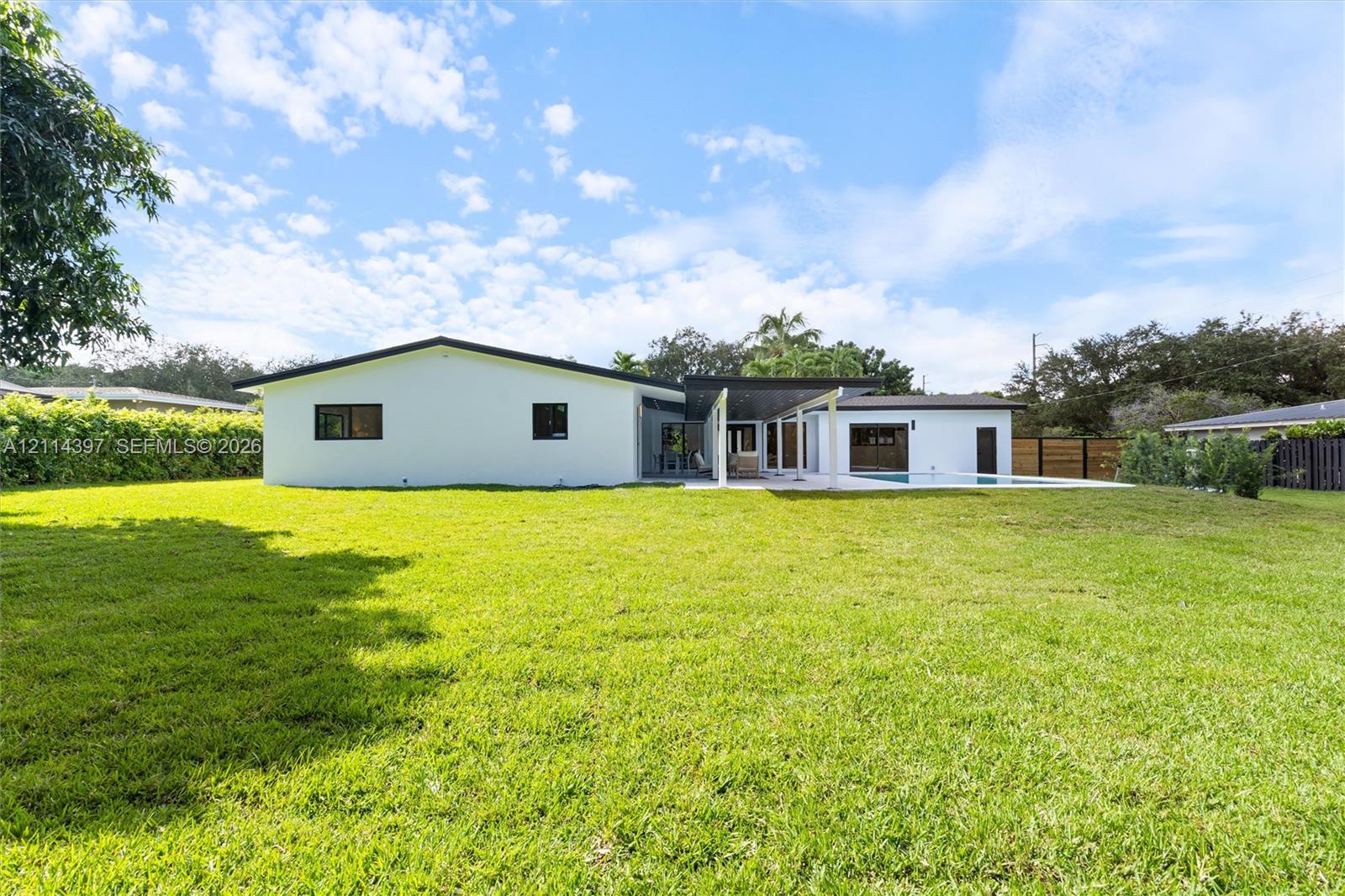 Expansive backyard featuring a sprawling lawn, swimming pool, covered patio, and perimeter privacy fencing