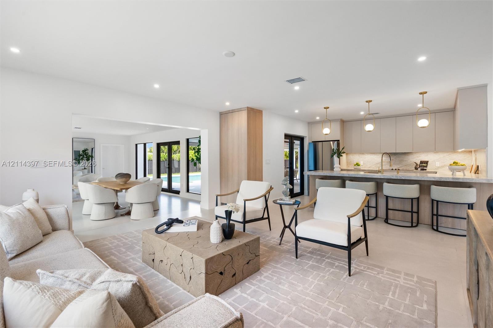 Open-concept interior featuring light-toned flooring, recessed lighting, a chef's kitchen with stone-surfaced countertops, custom flat-panel cabinetry, and multi-light pendant fixtures