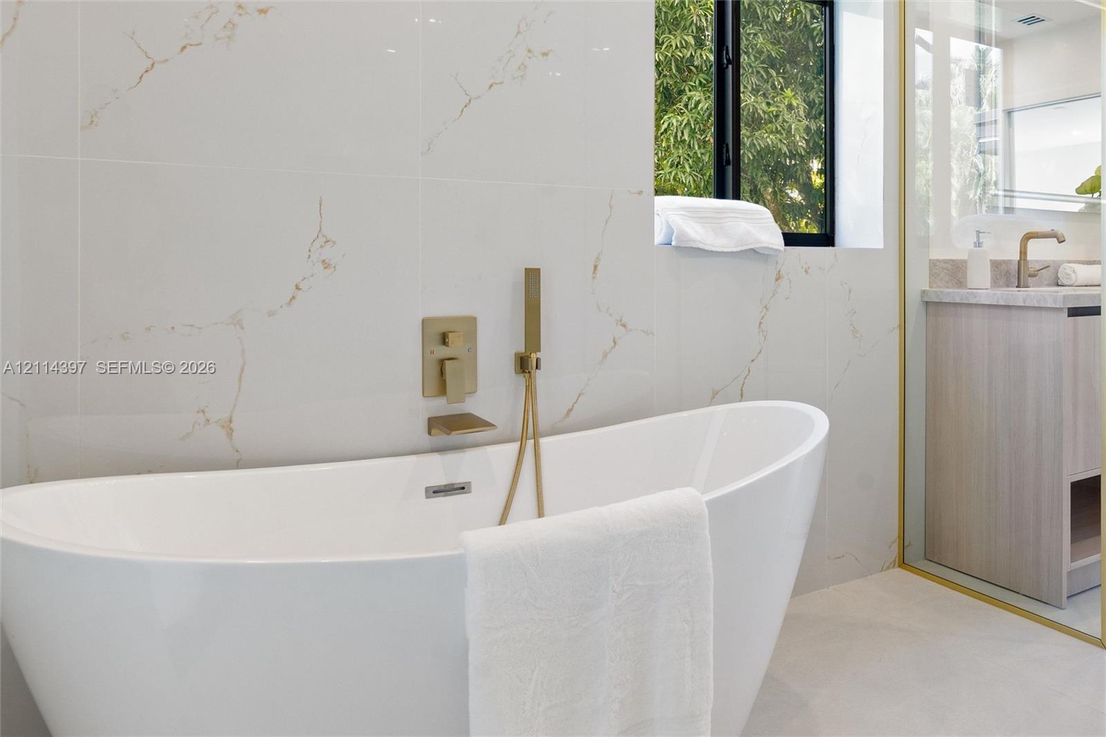 Freestanding soaking tub featuring wall-mounted metallic fixtures and a handheld shower spray, set against large-format tile walls with prominent veining
