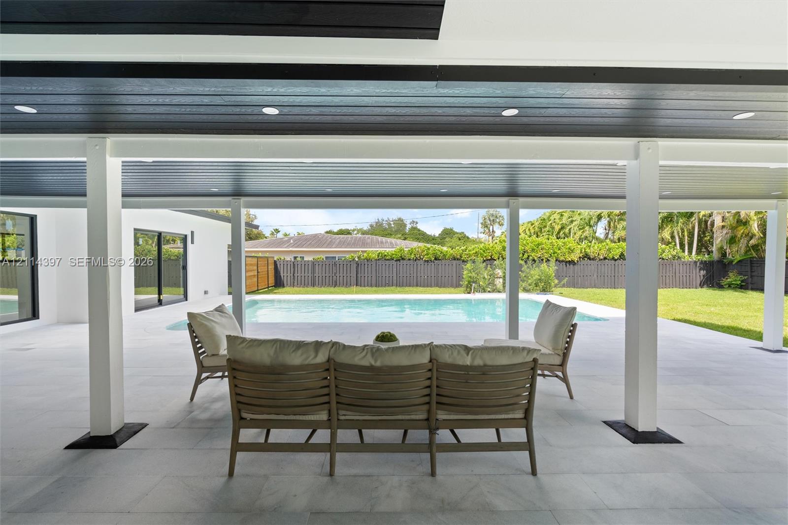 Covered patio with recessed lighting, tile flooring, and support columns, featuring a swimming pool and fenced backyard