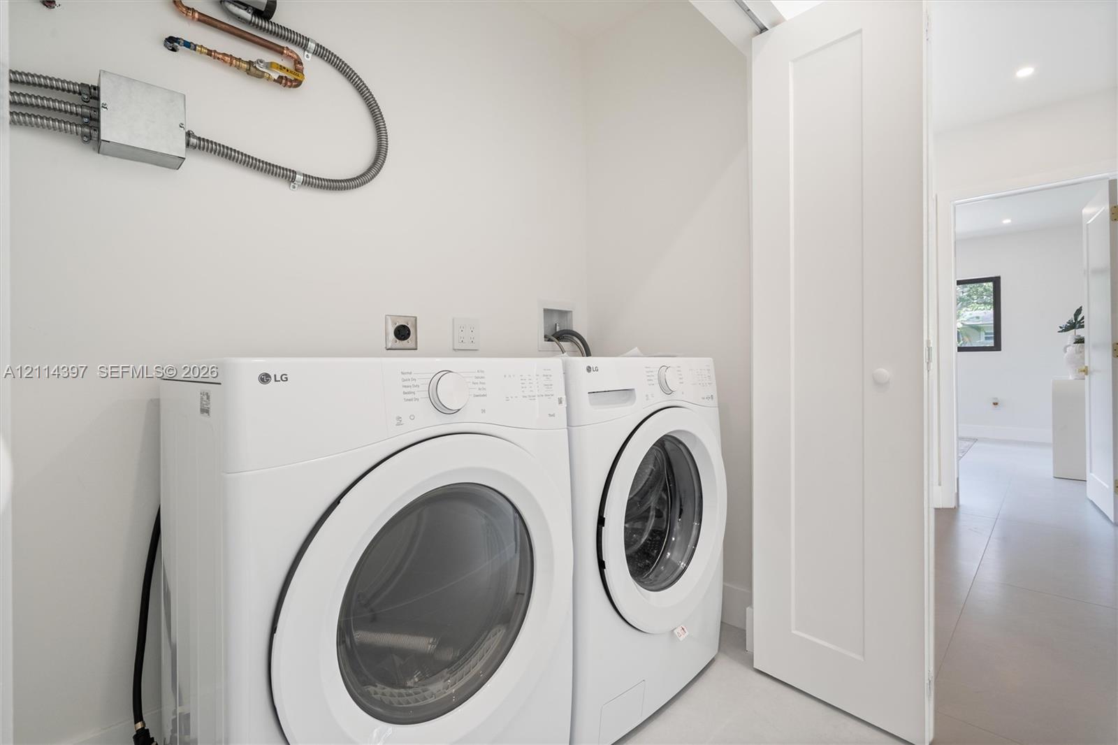 Laundry alcove featuring white front-loading appliances and neutral-toned tile flooring