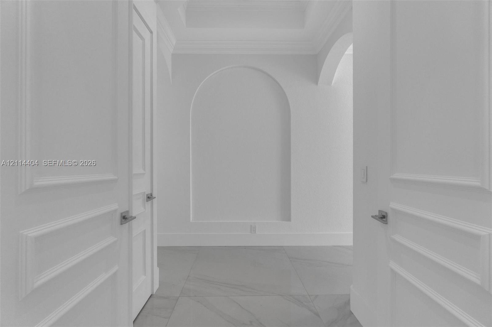 Interior featuring arched wall niche, coffered ceiling, oversized tile flooring, and paneled double doors with satin finish hardware
