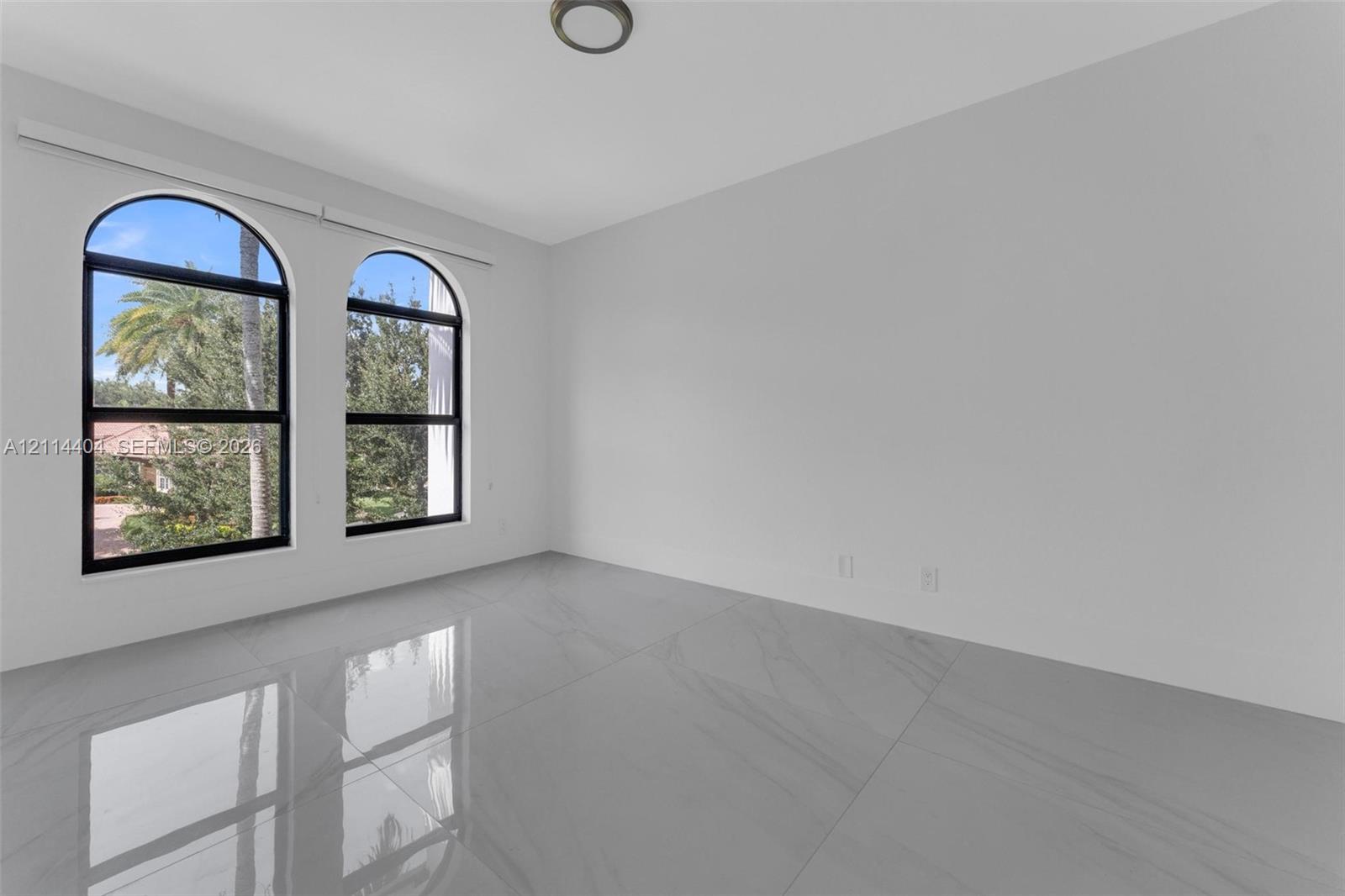 Spacious room featuring polished neutral-toned tile flooring, dual arched windows with black frames, and a flush-mount ceiling light
