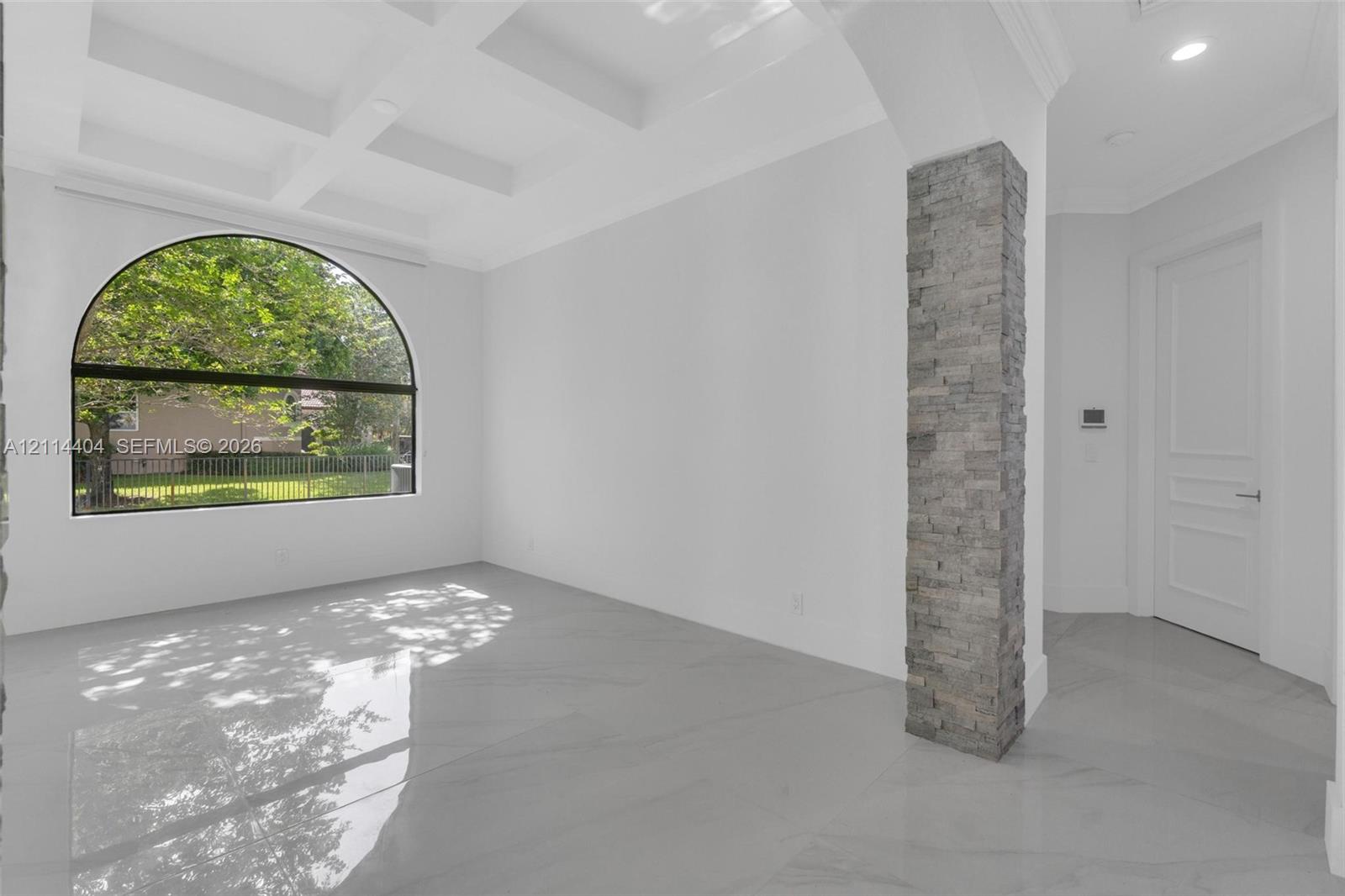 Coffered ceilings, large arched window, polished stone-finish flooring, and a decorative stacked-stone column
