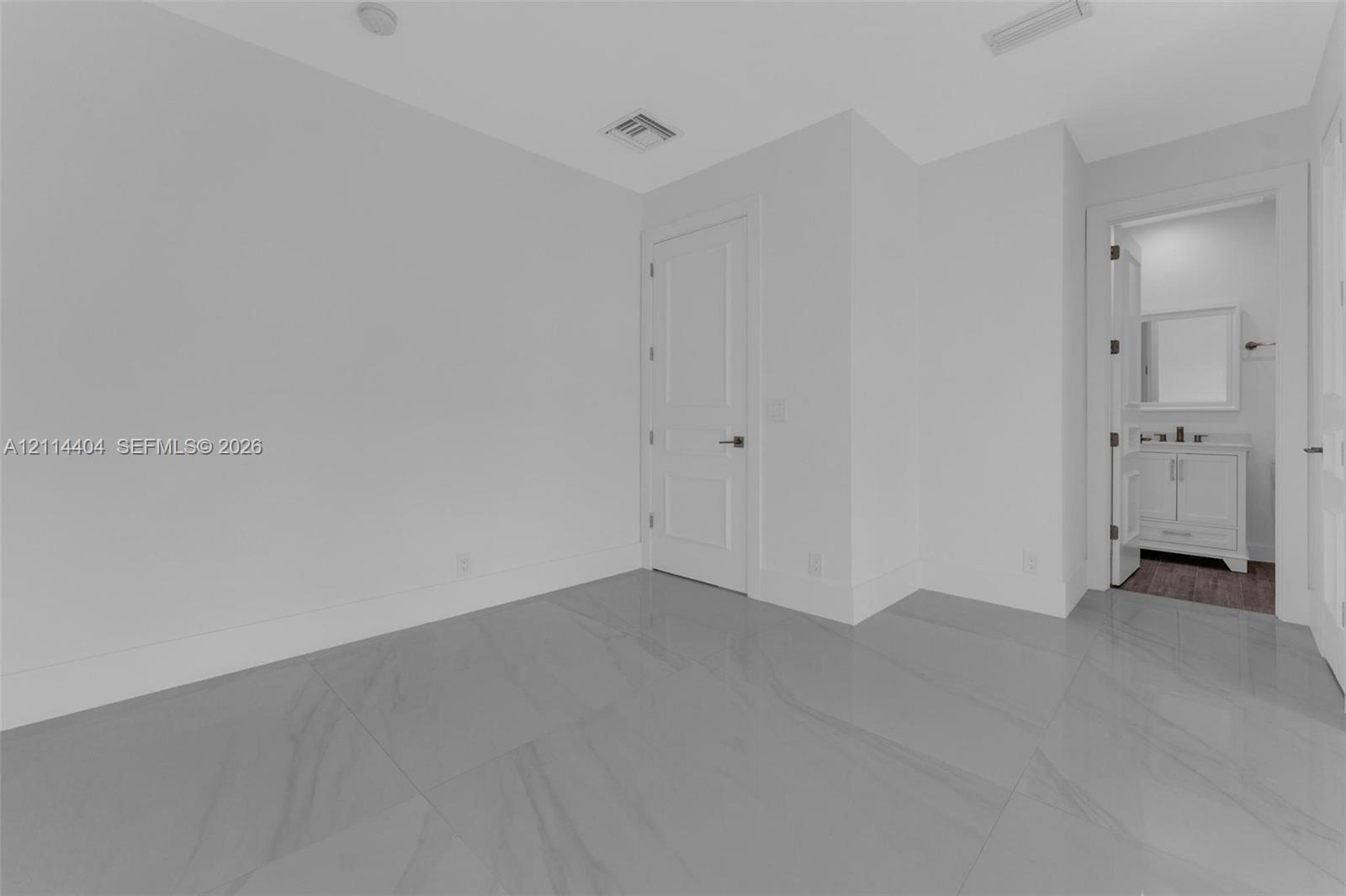 Neutral-toned room featuring large-format tile flooring, a multi-panel interior door, and smooth wall finishes