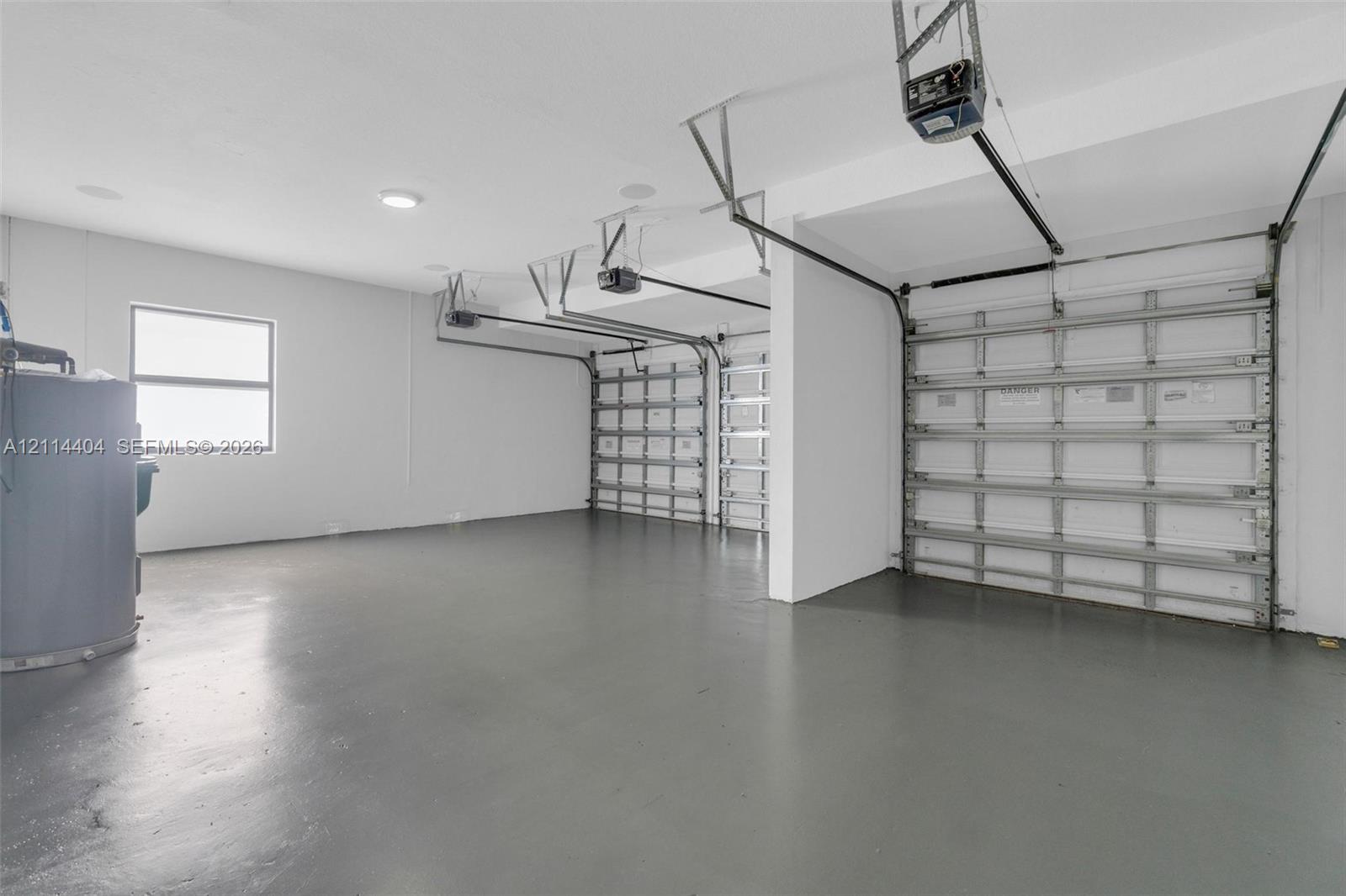 Three-car garage featuring a smooth-finished floor, white-painted walls, overhead garage door openers, and a dedicated window