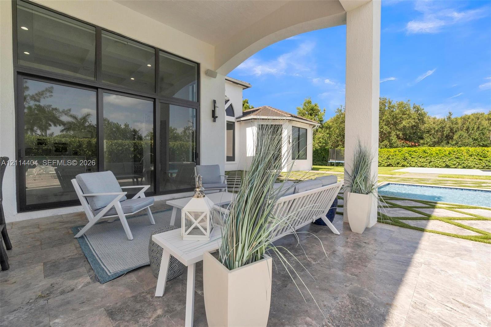 Covered lanai featuring natural stone flooring, expansive floor-to-ceiling multi-panel glass doors, recessed lighting, and a geometric-patterned hardscape surrounding a swimming pool