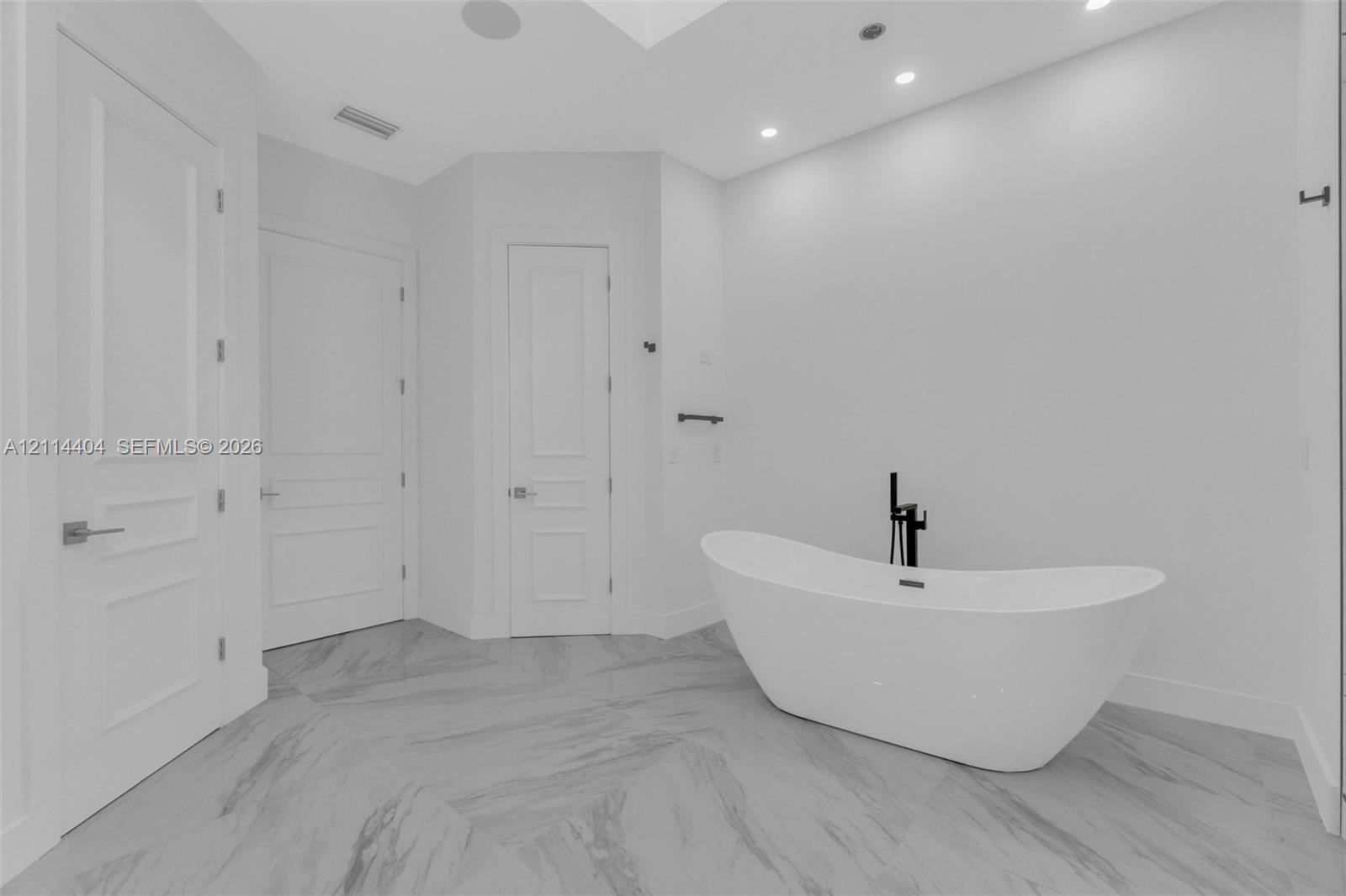 Freestanding soaking tub with matte black floor-mounted faucet, large-format tile flooring, recessed lighting, and multi-panel solid core doors