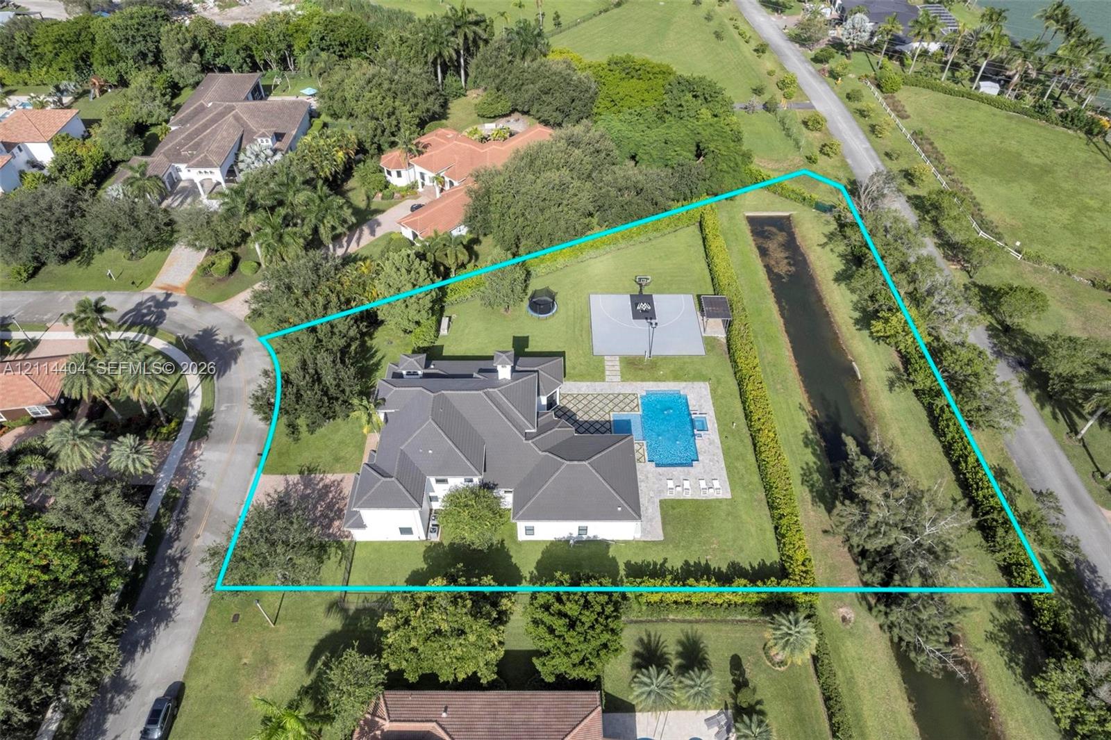 Aerial view of property featuring a sprawling lot, private swimming pool, paved patio, multi-purpose sports court, and manicured landscaping