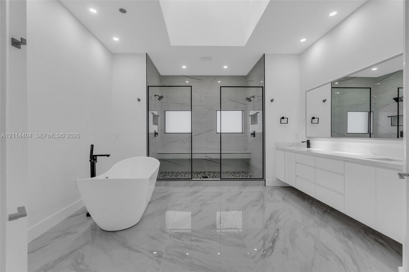 Freestanding soaking tub with matte black faucet, walk-in shower with dual shower heads and glass enclosure, floating dual-sink vanity, and large-format tile flooring