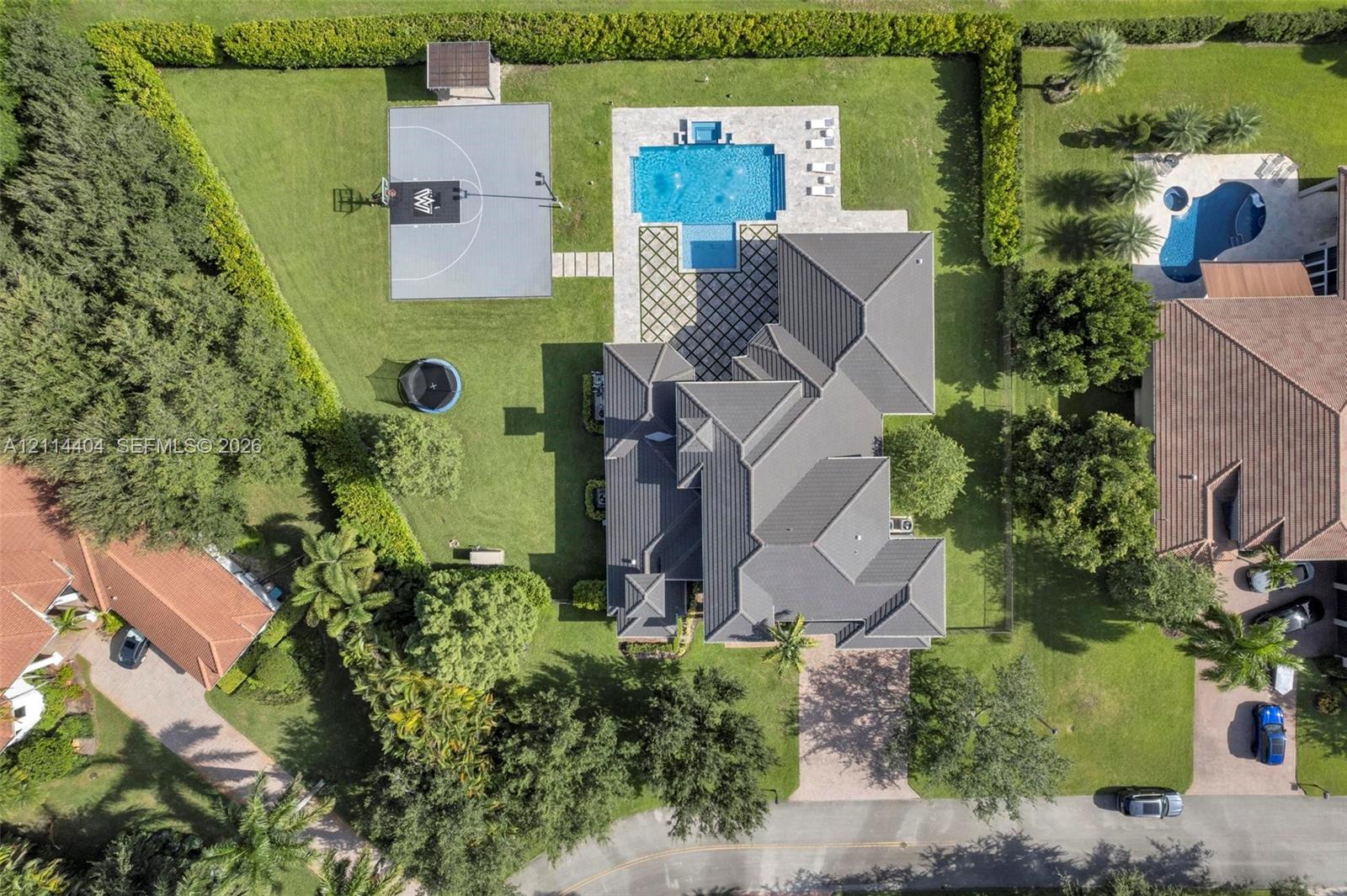 Aerial perspective of a sprawling property featuring a multi-hipped roof, a swimming pool with stone-patterned decking, and a dedicated sport court