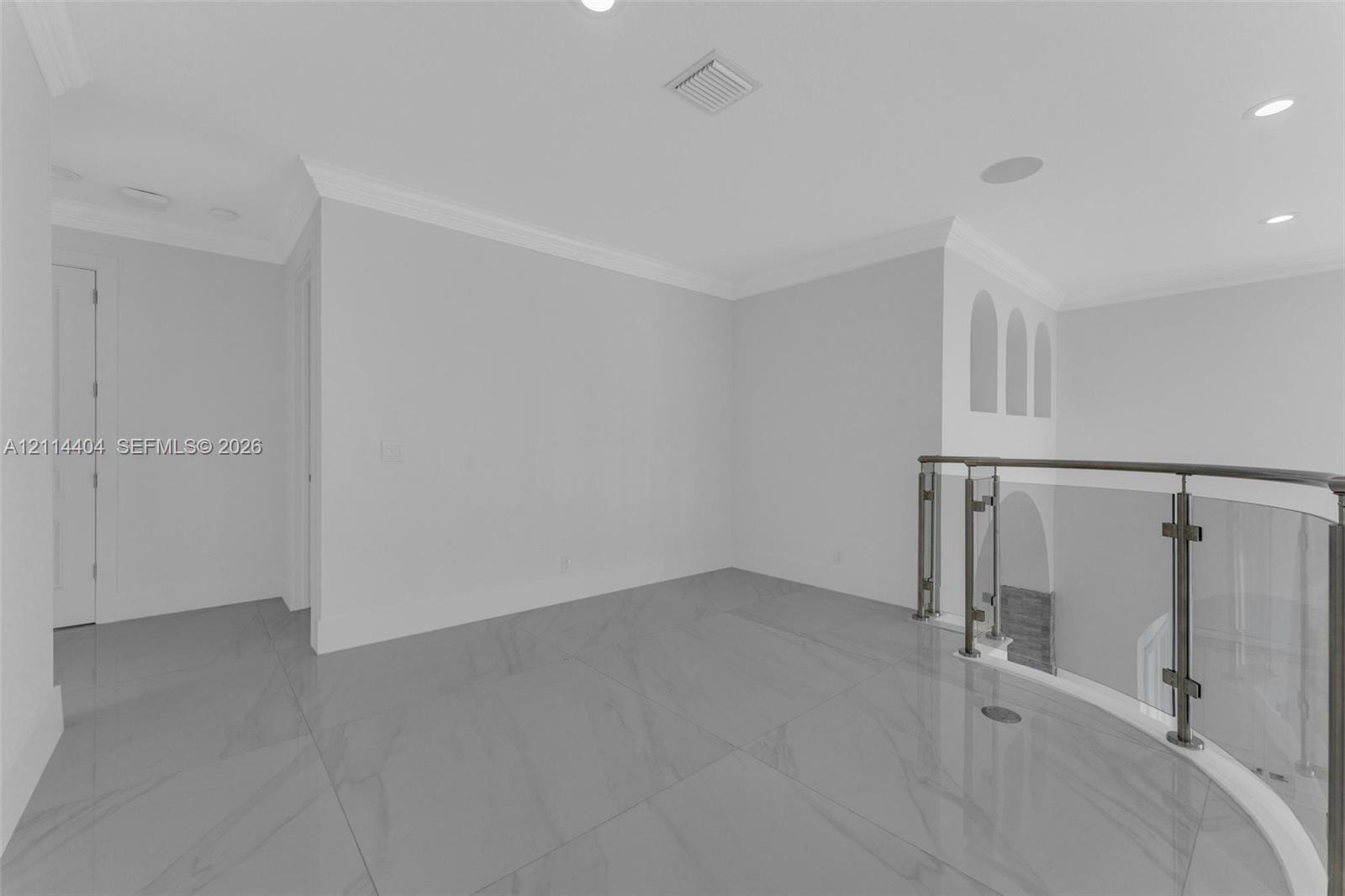 Large-format tile flooring, glass-panel railing with metal hardware, crown molding, recessed lighting, and arched wall niches
