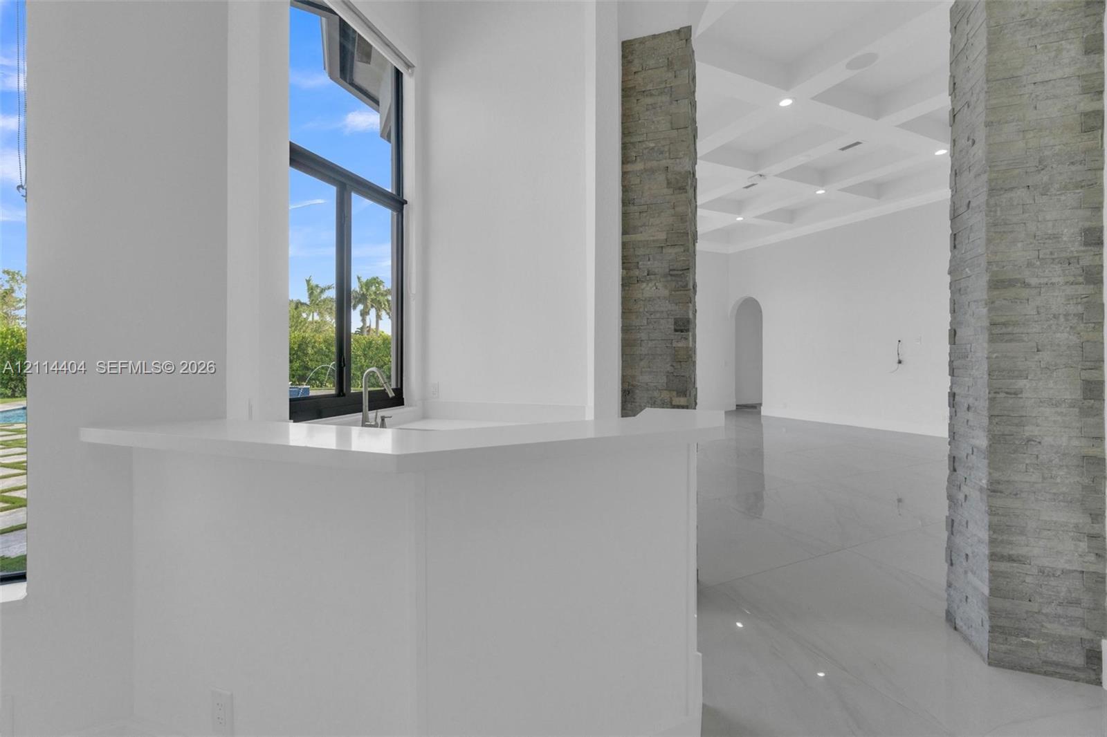 Interior space featuring coffered ceilings, stacked stone columns, porcelain-finish flooring, and a stone-topped bar with an integrated sink