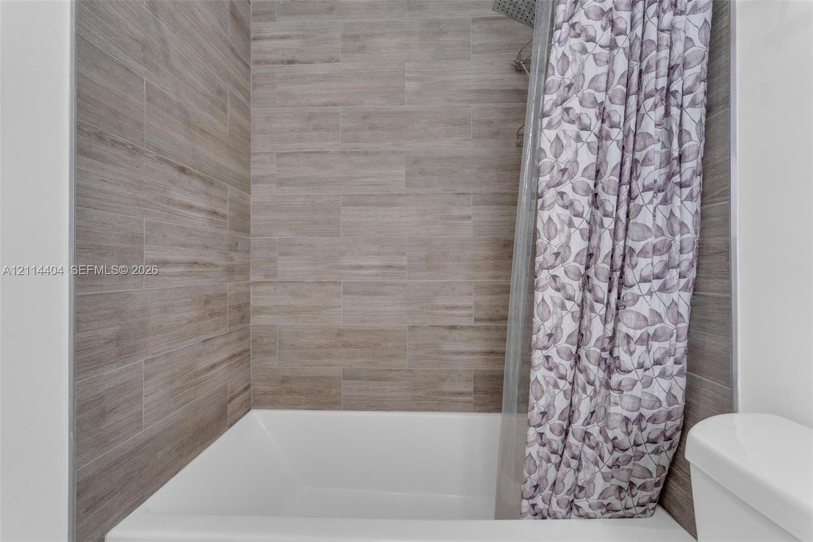 Bathtub surround featuring light-toned, horizontal tile with a wood-finish texture and metallic edge trim