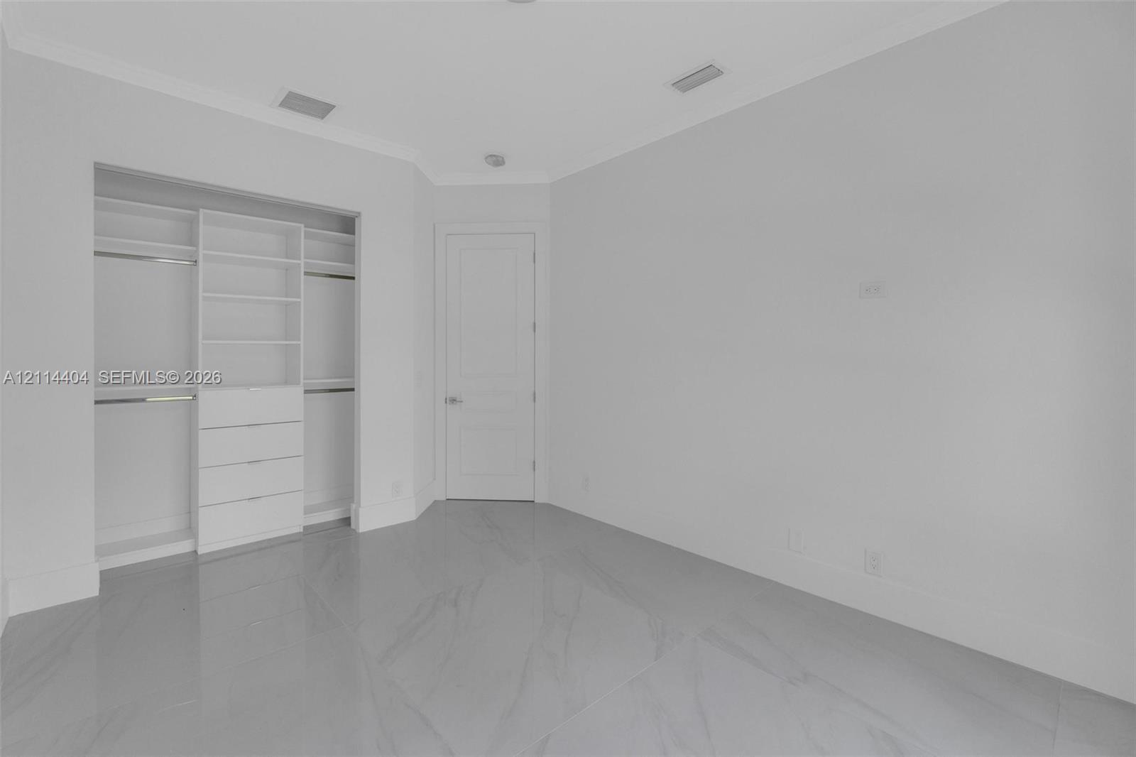 Neutral-toned room featuring large-format tile flooring, built-in closet organization with drawers and shelving, crown molding, and a paneled interior door