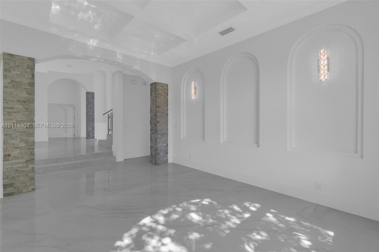 Large-format tile flooring, recessed wall niches, decorative stone-veneer columns, and wall-mounted light fixtures