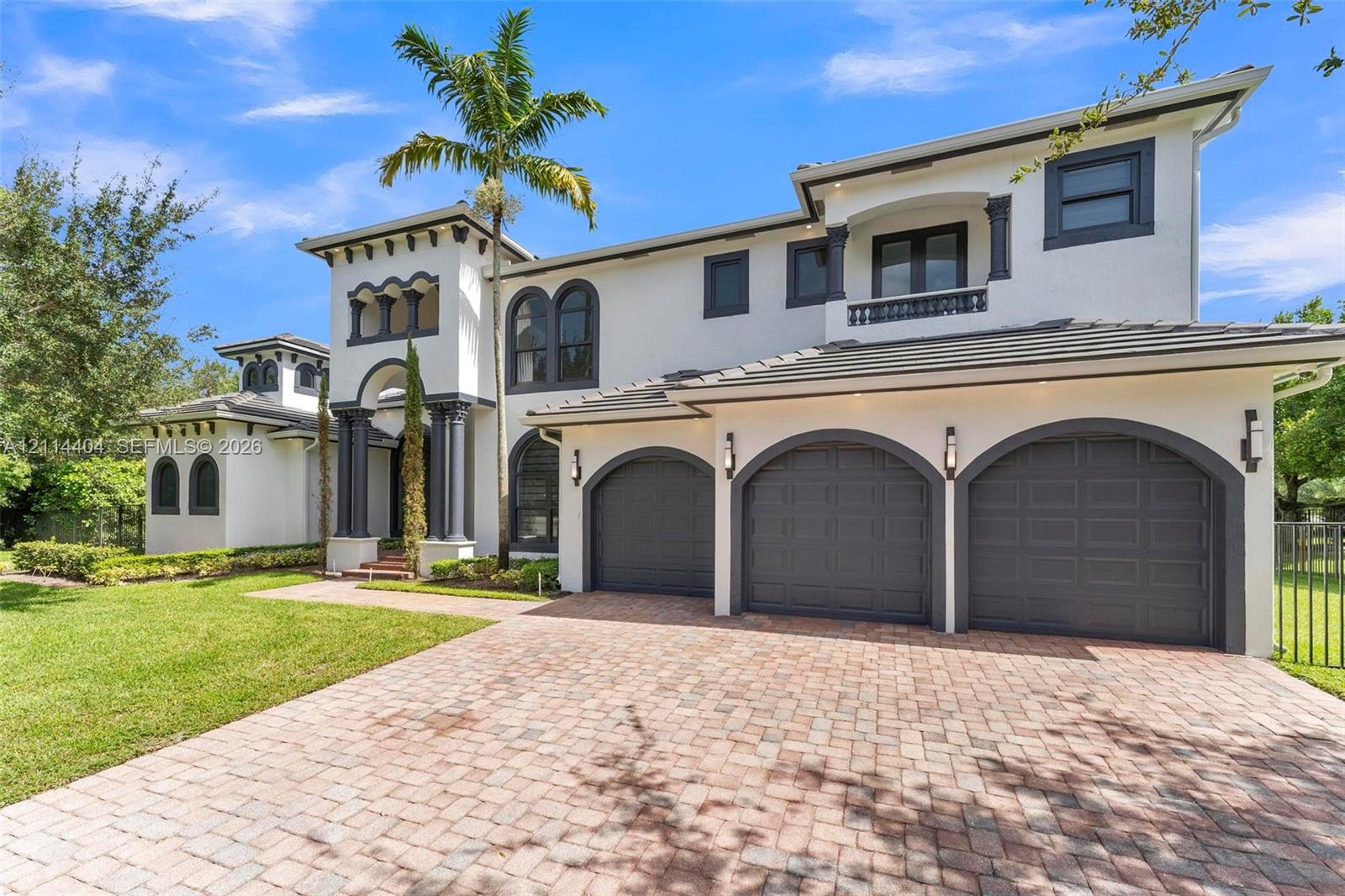 Mediterranean-inspired exterior featuring stucco facade, arched garage bays, decorative columns, arched window detailing, and a paver driveway