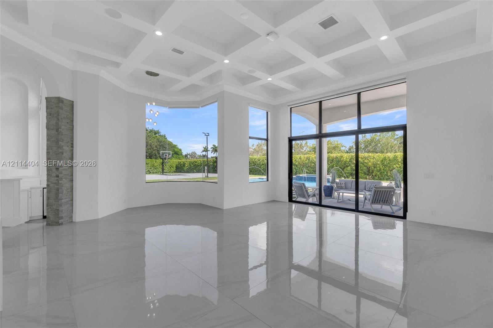 Coffered ceiling, polished stone-finish flooring, floor-to-ceiling windows, stacked stone pillar accents, and sliding glass wall system