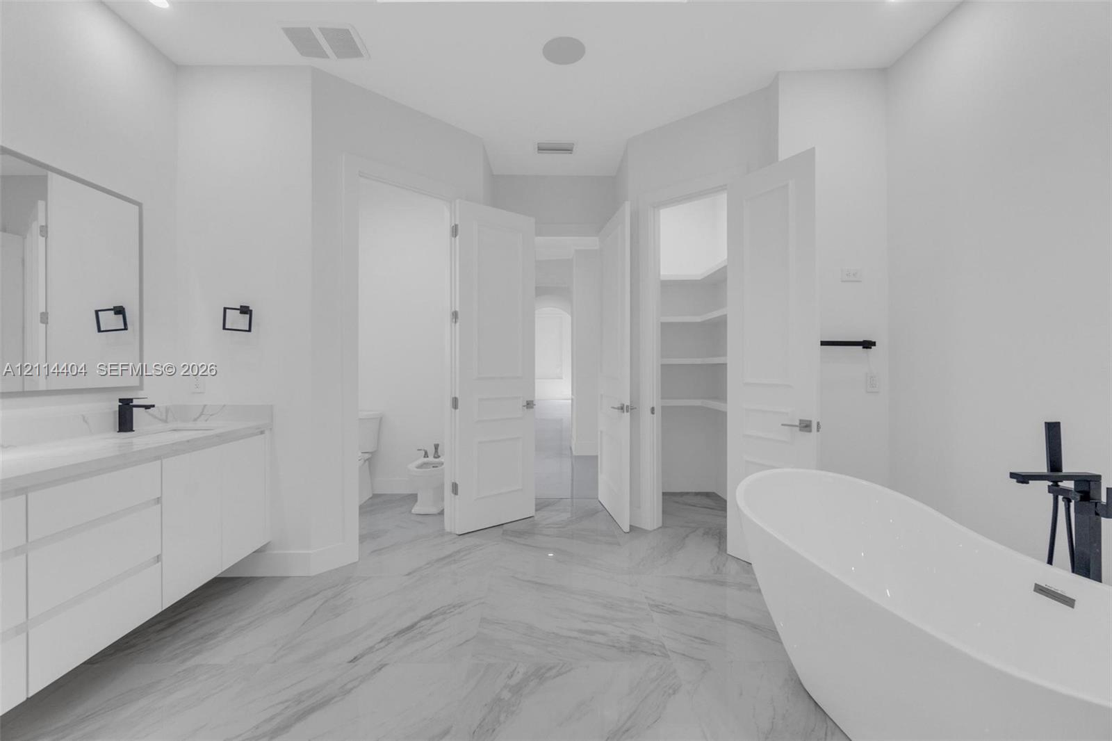 Bathroom featuring a freestanding soaking tub with matte black floor-mounted faucet, floating vanity with dual sinks, built-in shelving, and large-format tile flooring