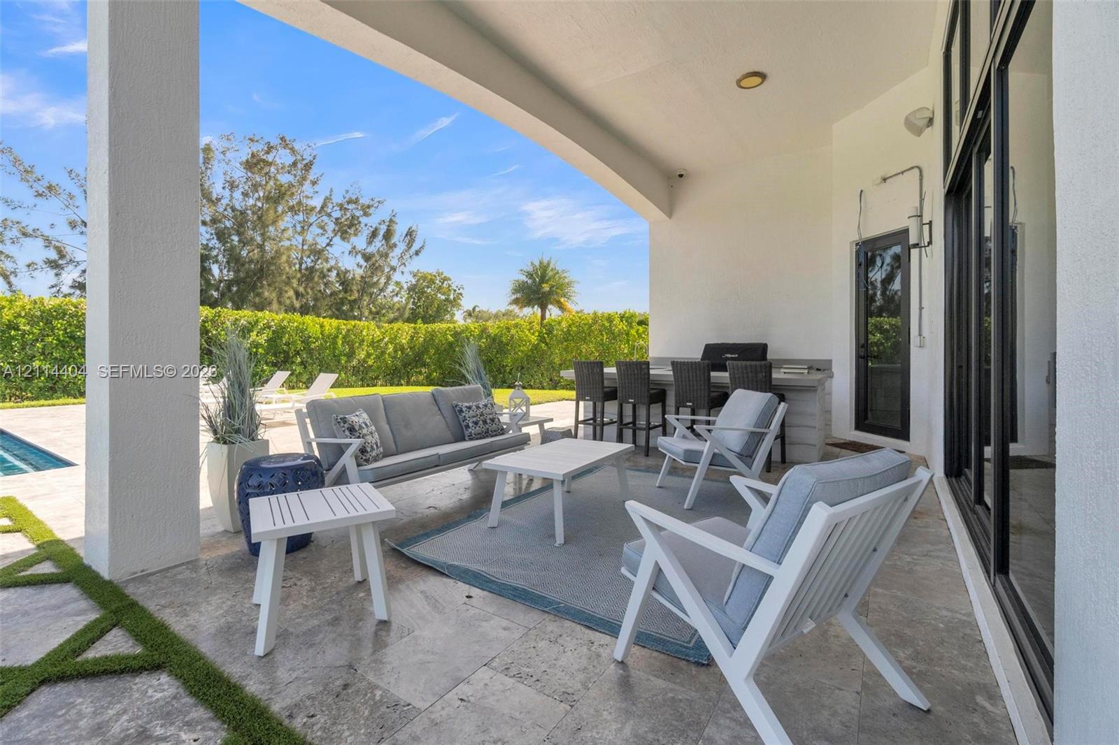Covered patio featuring stone-tile flooring, a built-in outdoor kitchen with a bar counter, and expansive glass sliding doors
