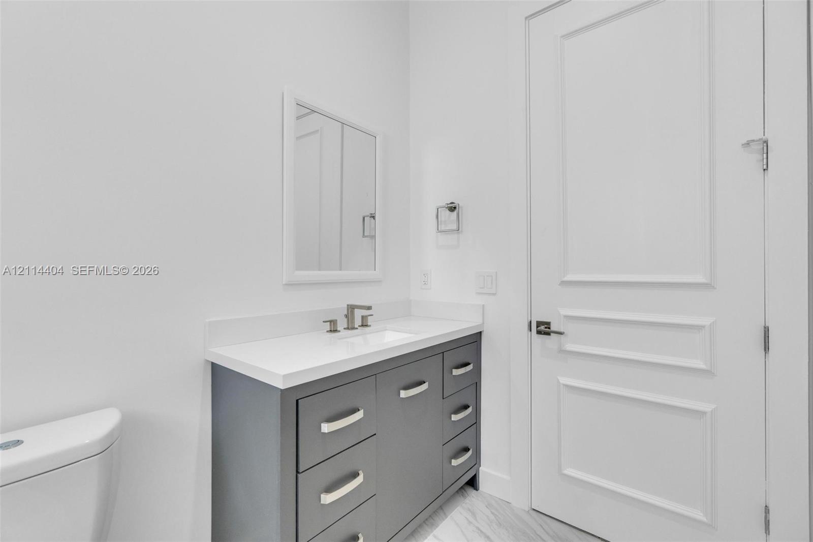 Grey vanity with stone countertop, rectangular undermount sink, widespread faucet, framed mirror, and multi-panel solid interior door