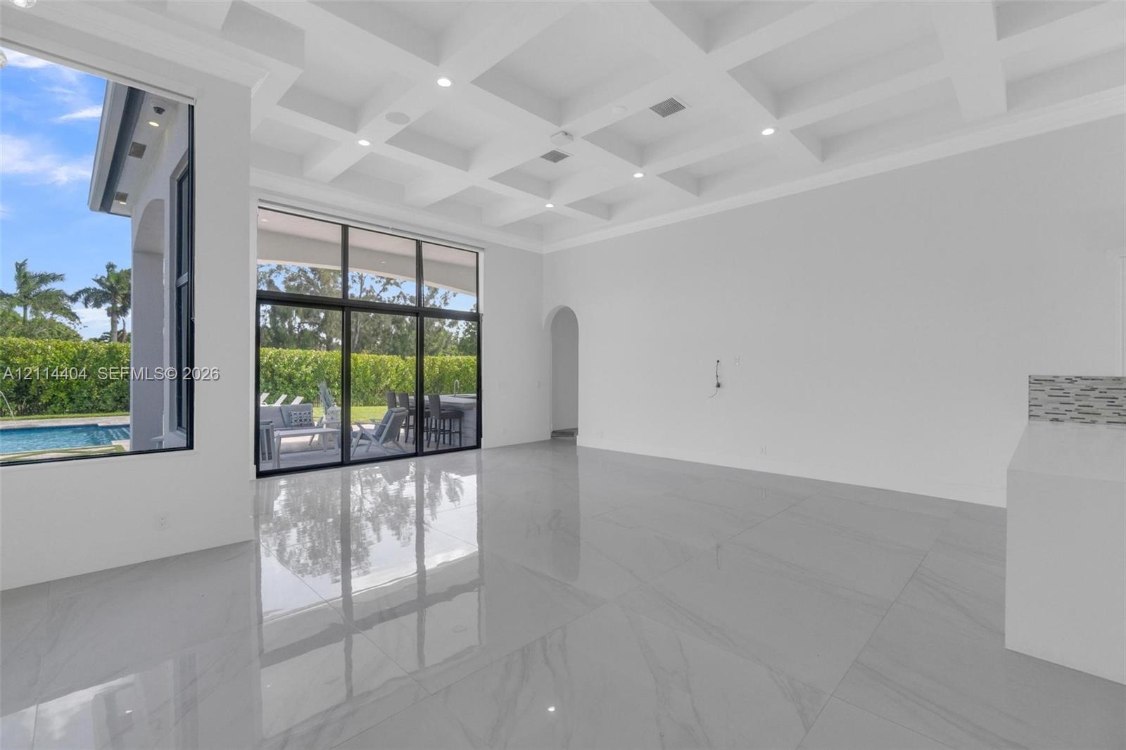 Coffered ceilings, large-format tile flooring, floor-to-ceiling glass sliding doors, and recessed lighting