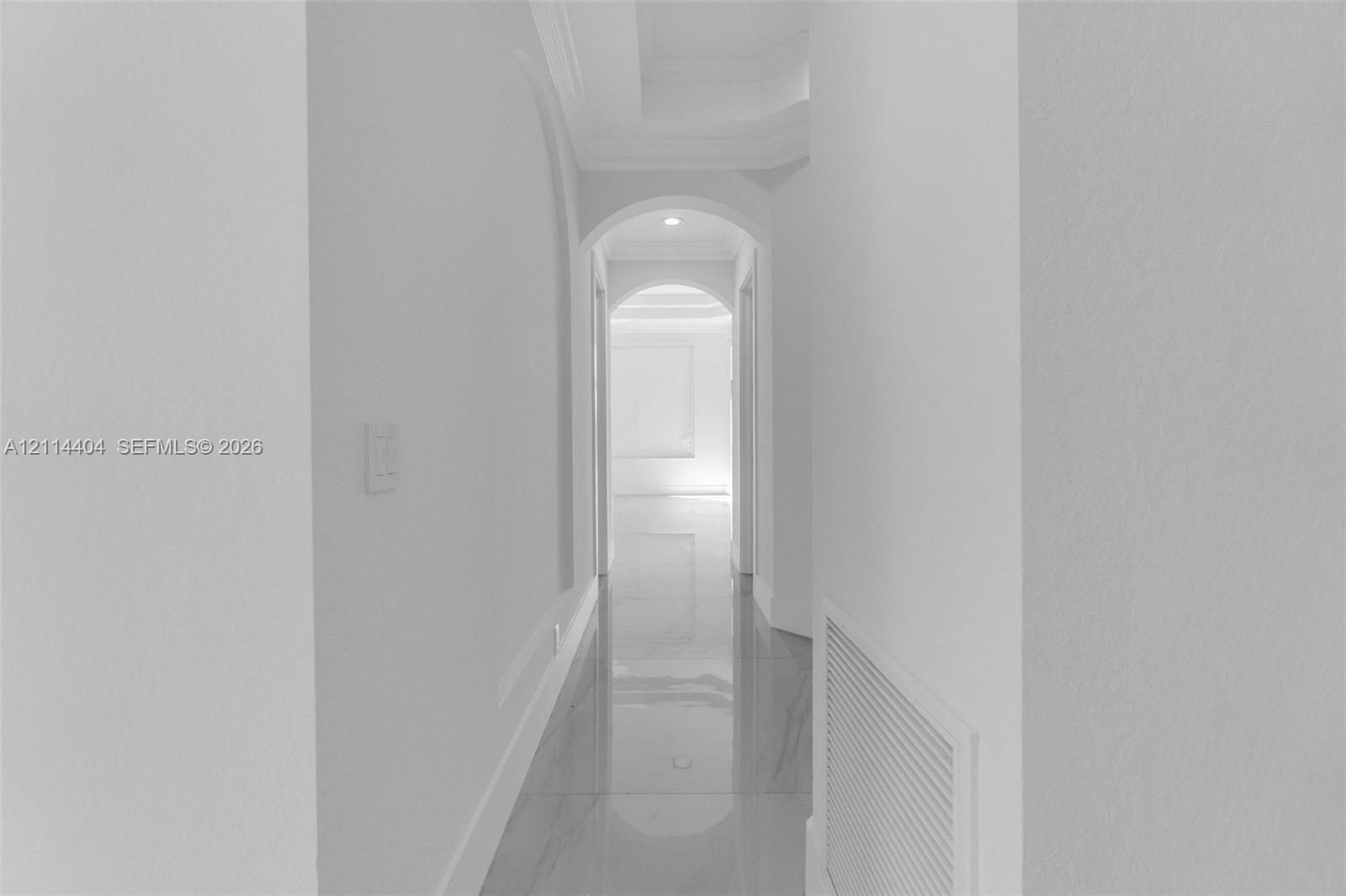 Hallway featuring arched architectural detailing, recessed ceiling lighting, and polished stone-finish flooring