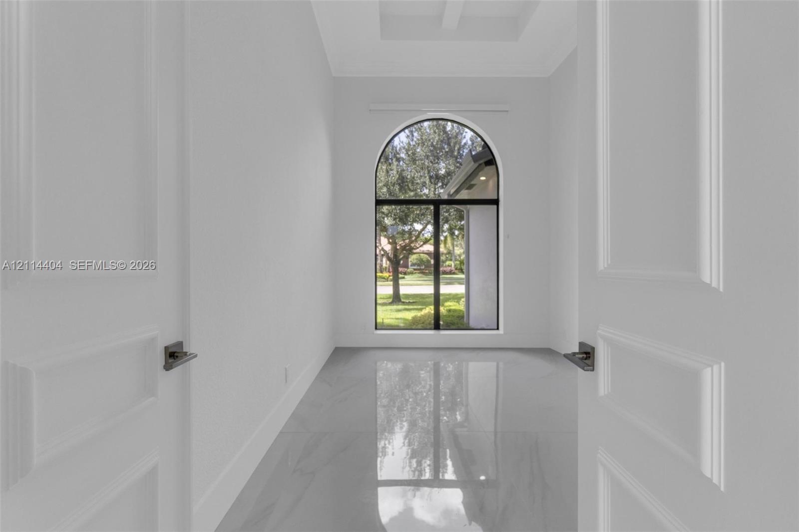 Double-door entry featuring polished stone flooring, a tray ceiling, and an arched window with a black frame