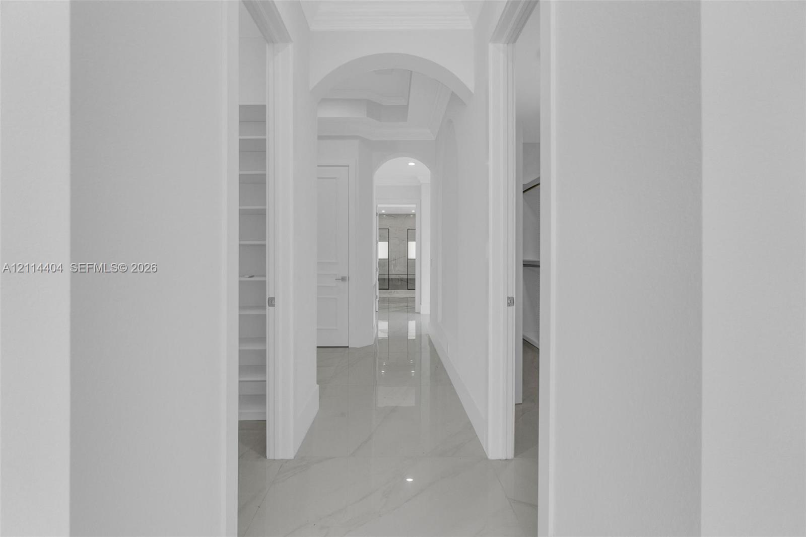 Hallway featuring porcelain tile flooring, architectural arched doorways, crown molding, and built-in shelving