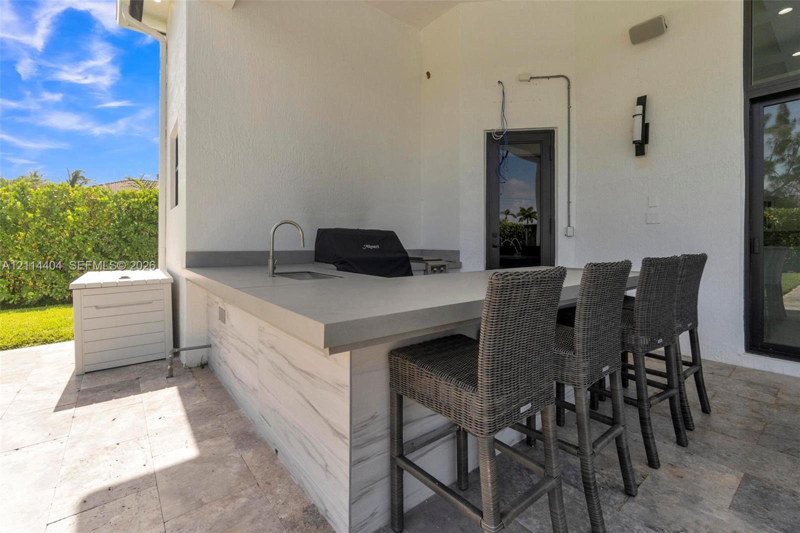Covered outdoor kitchen featuring stone-finish patio flooring, built-in counter with integrated sink, and wall-mounted exterior lighting
