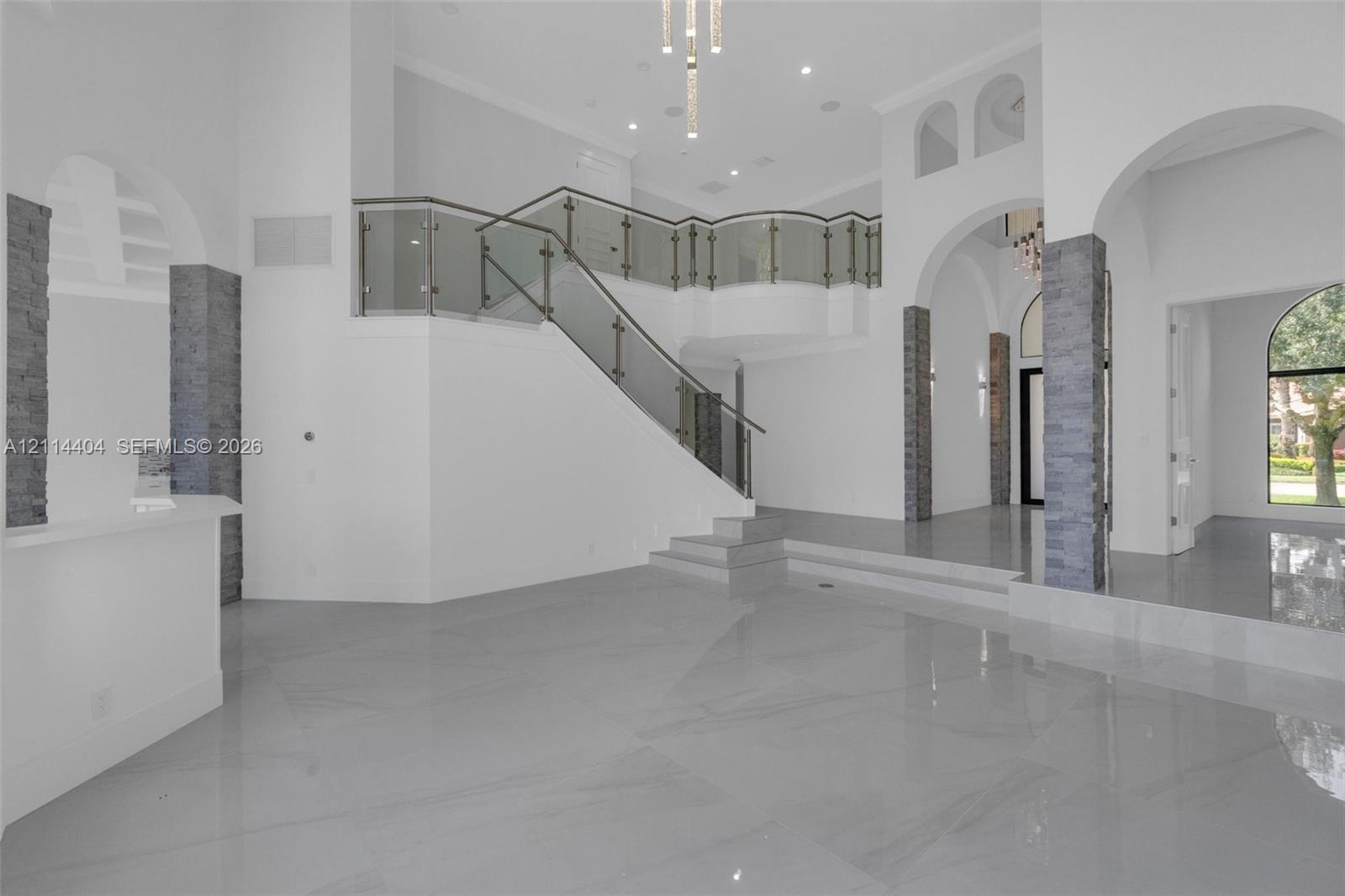 Grand foyer featuring large-format tile flooring, tiered levels, architectural stone-veneer pillars, glass-panel railings, and arched entryways Grand foyer featuring large-format tile flooring, tiered levels, architectural stone-veneer pillars, glass-panel railings, and arched entryways