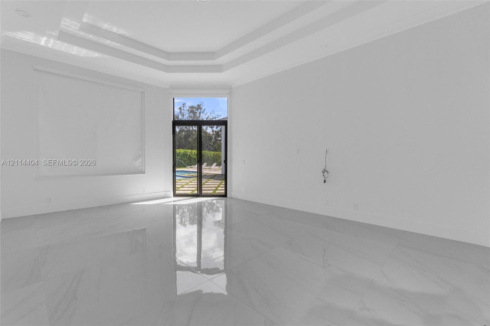 Expansive living area featuring polished large-format tile flooring, a multi-tiered tray ceiling, and sliding glass doors with dark frames providing exterior access