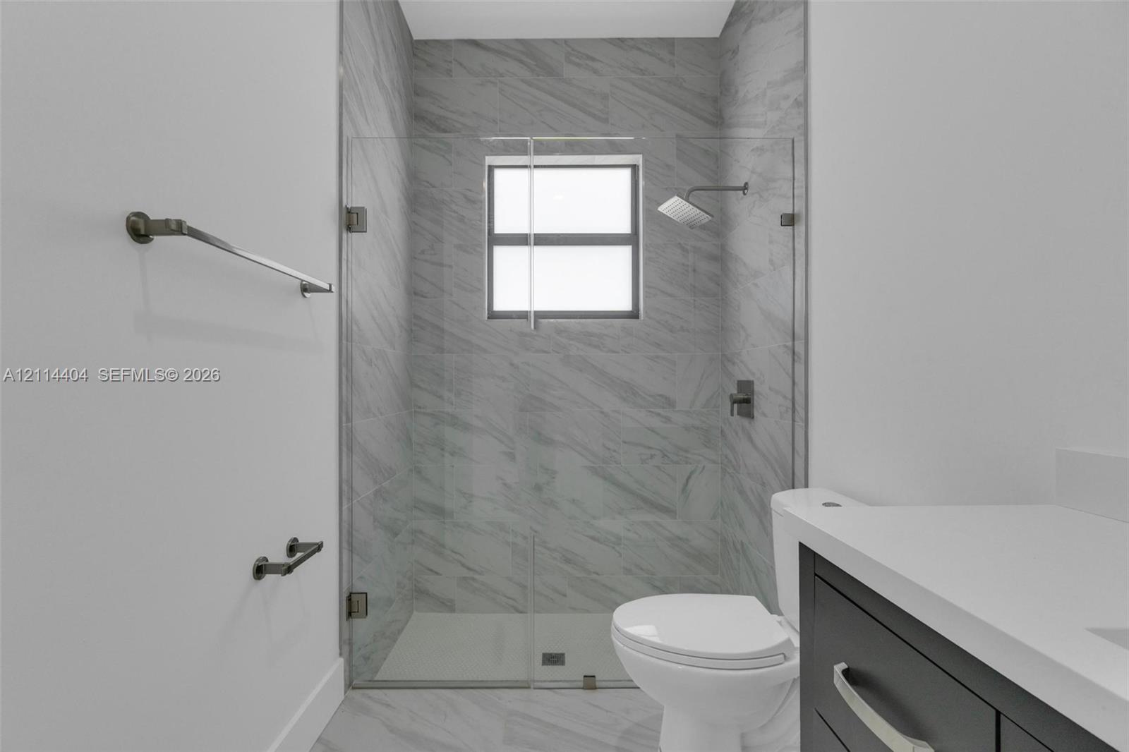 Walk-in shower with floor-to-ceiling neutral tile, frameless glass enclosure, dark-finish rainfall shower head, and dark-finish hardware