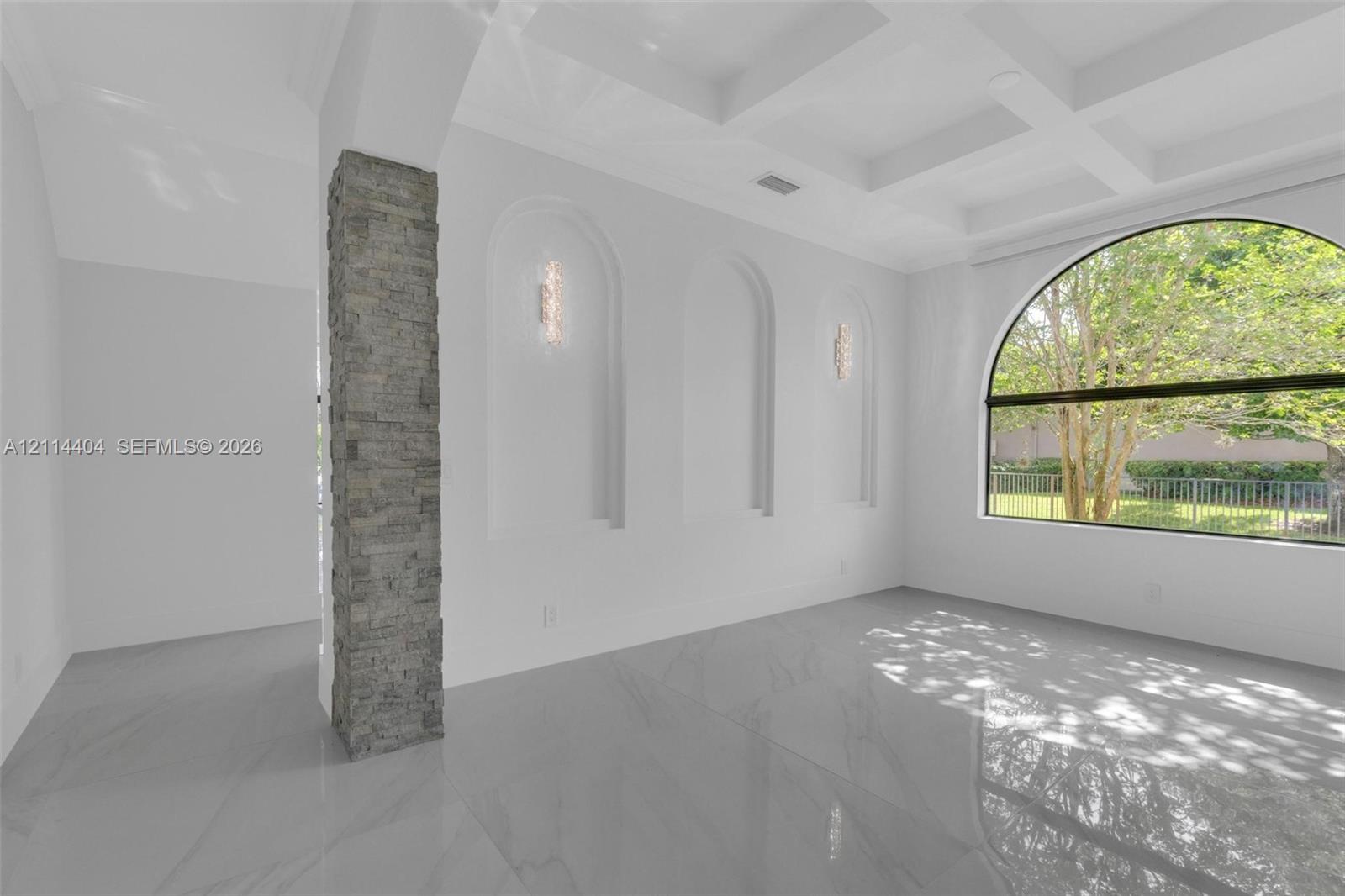 Interior space featuring a coffered ceiling, large arched window, stone-finished column, and three recessed arched alcoves with wall-mounted lighting
