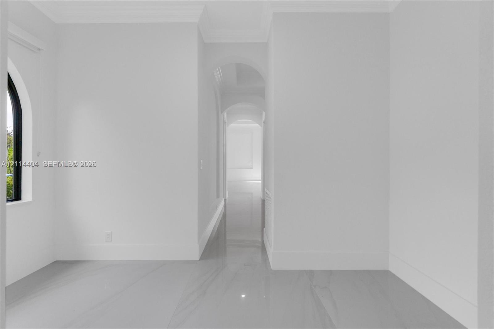 Interior space featuring arched doorways, polished stone-finish flooring, a black-framed arched window, and crown molding